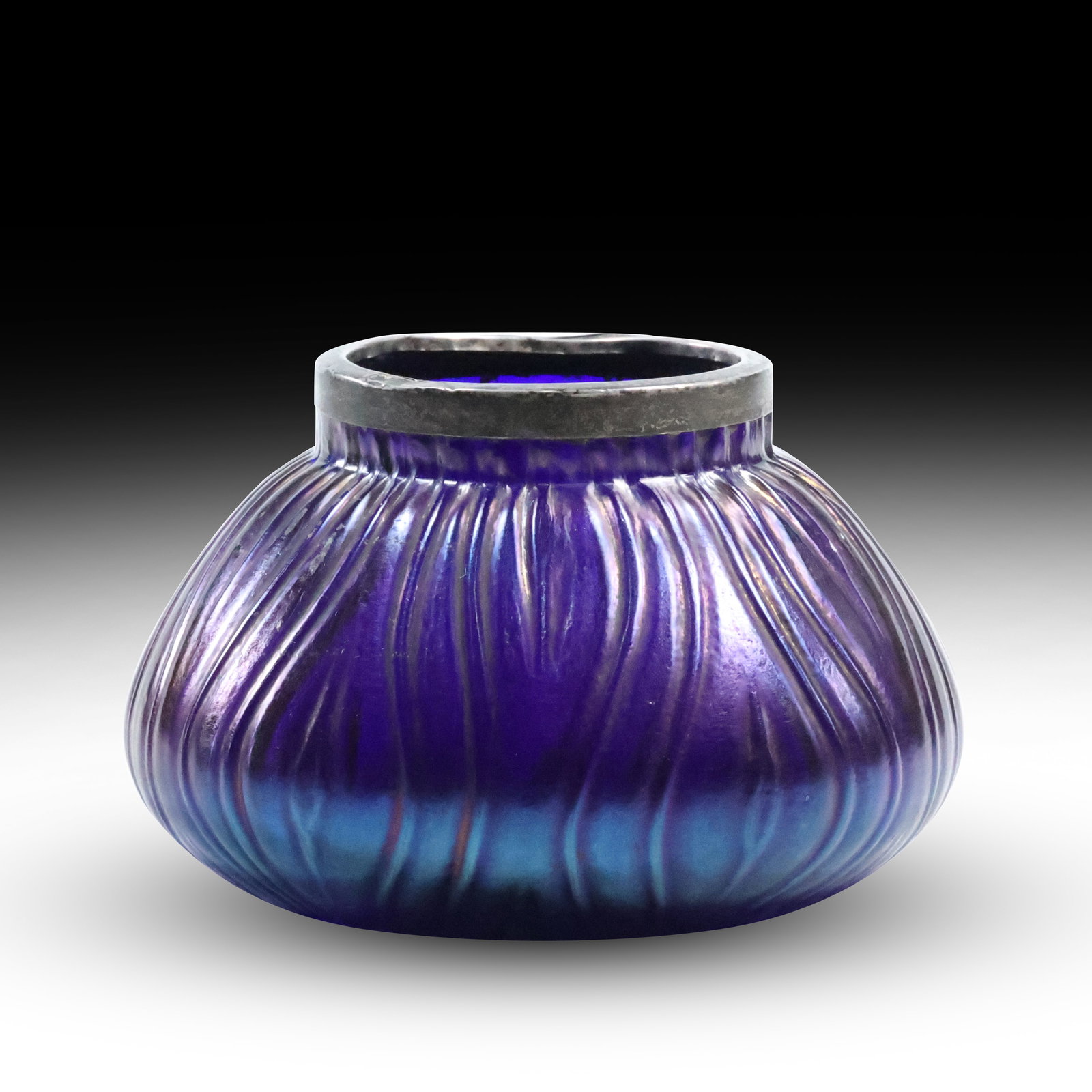 Loetz Style Iridescent Art Glass Vase with Hammered Metal Rim: Step into the elegance of Art Nouveau with this exquisite iridescent art glass vase, inspired by the iconic works of Loetz. This captivating piece showcases a mesmerizing ribbed and ripple pattern, wi