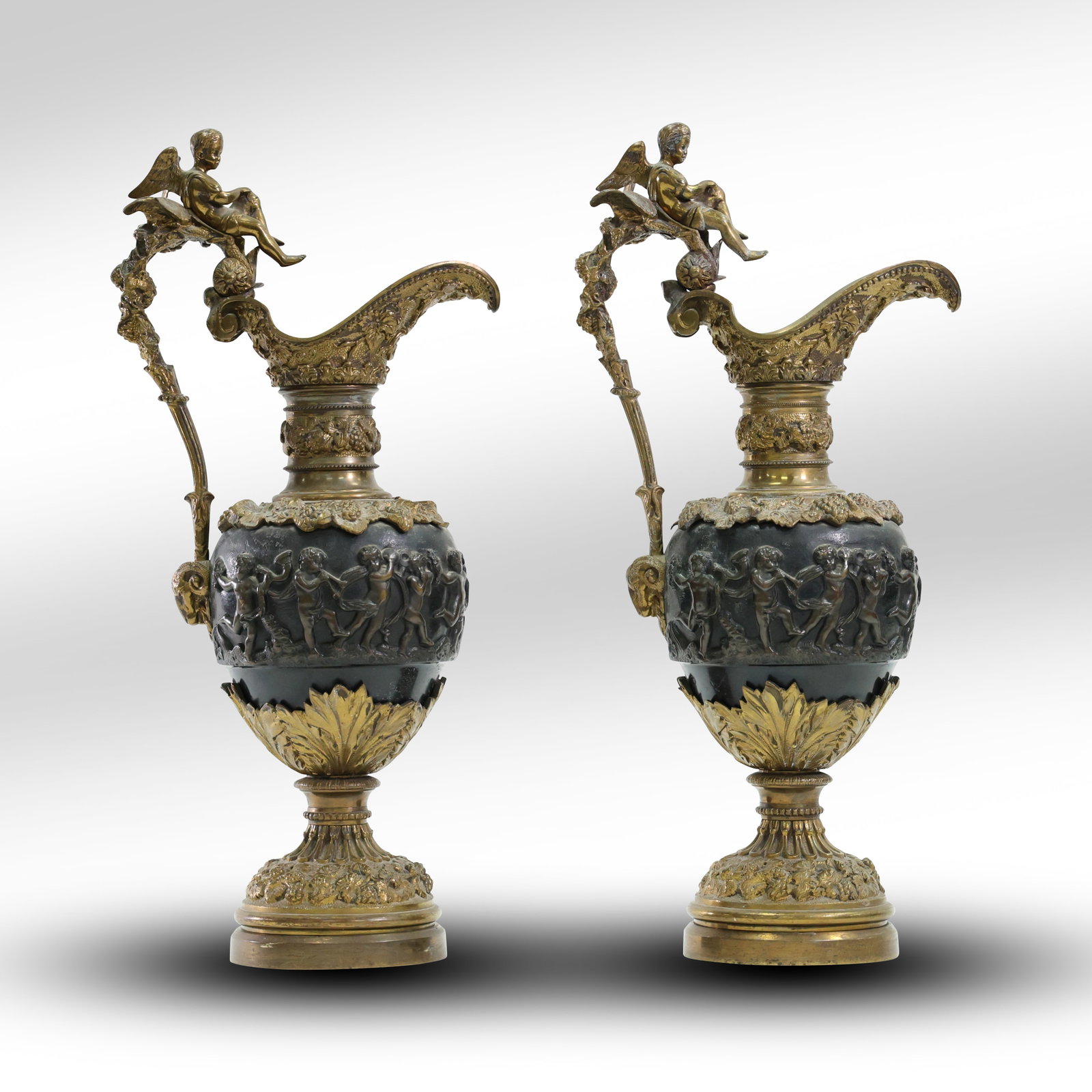 Pair of Gilt and Patinated Bronze Ewers: Maison Giroux , Relief of Dancing Cherubs: This magnificent pair of gilt and patinated bronze ewers, attributed to Maison Giroux, features a tapering ovoid body adorned with a finely cast patinated bronze band depicting a Bacchic procession of