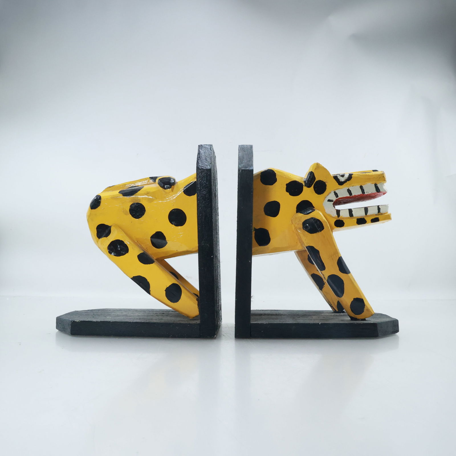 Novelty Wooden Stylized Caricature Leopard Bookends Hand Painted: pair of bookends featuring a stylized leopard Each bookend displays one half of the animal, with a yellow body covered in black spots. The exaggerated features include a wide-open mouth with prominent