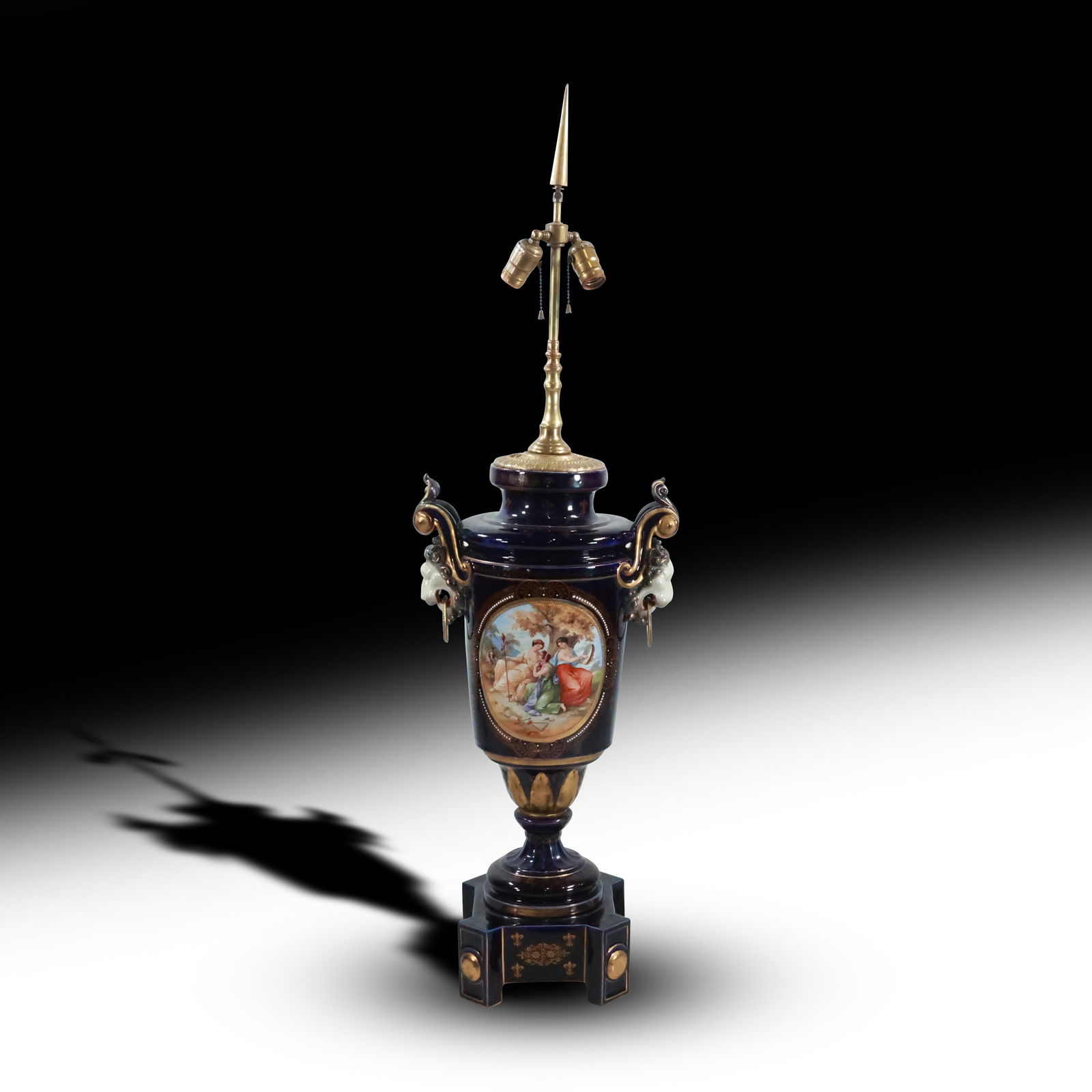 Royal Vienna Porcelain Covered Urn Lamp – Gilt Decorated Cobalt and Polychrome Porcelain: This exquisite Royal Vienna porcelain covered urn, now presented as a lamp, is a masterful blend of artistry and elegance. The urn, richly decorated in gilt and cobalt, is adorned with intricate polyc