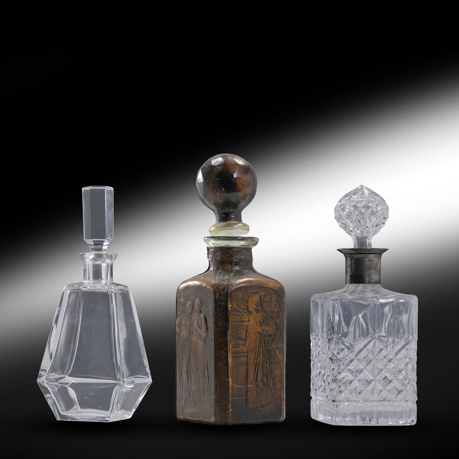 2 Vintage Liquor Decanters:[1] Leather Cased with Reief Figures, [2] Crystal Glass with Stoppers: 2 Vintage Liquor Decanters:[1] Leather Cased with Reief Figures, [2] Crystal Glass with Stoppers. size: 11 x 5 x 5, 10 x 3.5