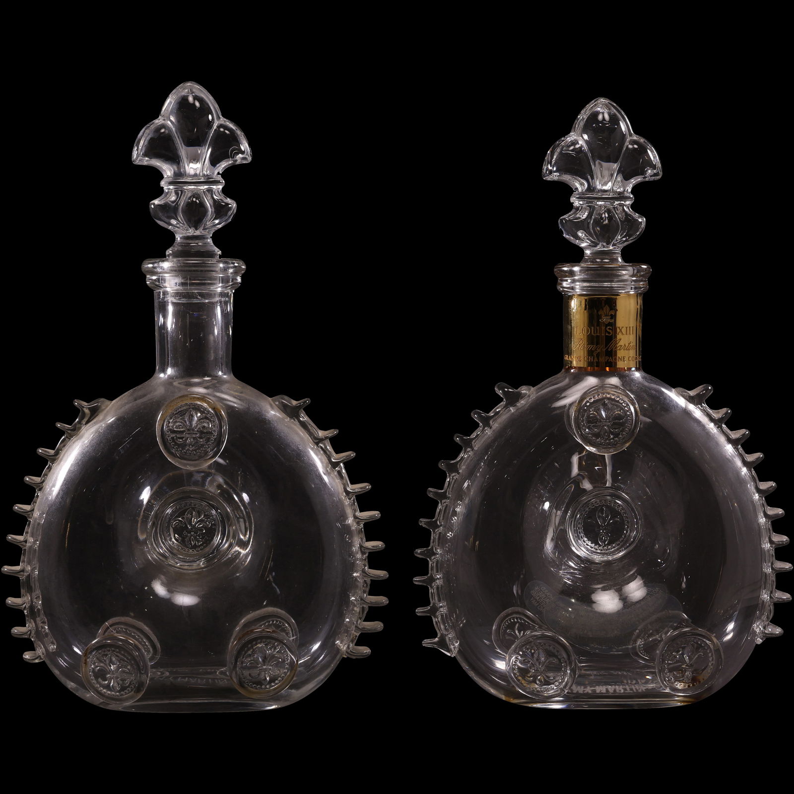 Pair of Rémy Martin Louis XIII Cognac Baccarat Crystal Decanters: Pair of Rémy Martin Louis XIII Cognac decanters crafted by Baccarat Crystal. Each features the signature circular form with scalloped edges and applied fleur-de-lis motifs, along with the distinctive