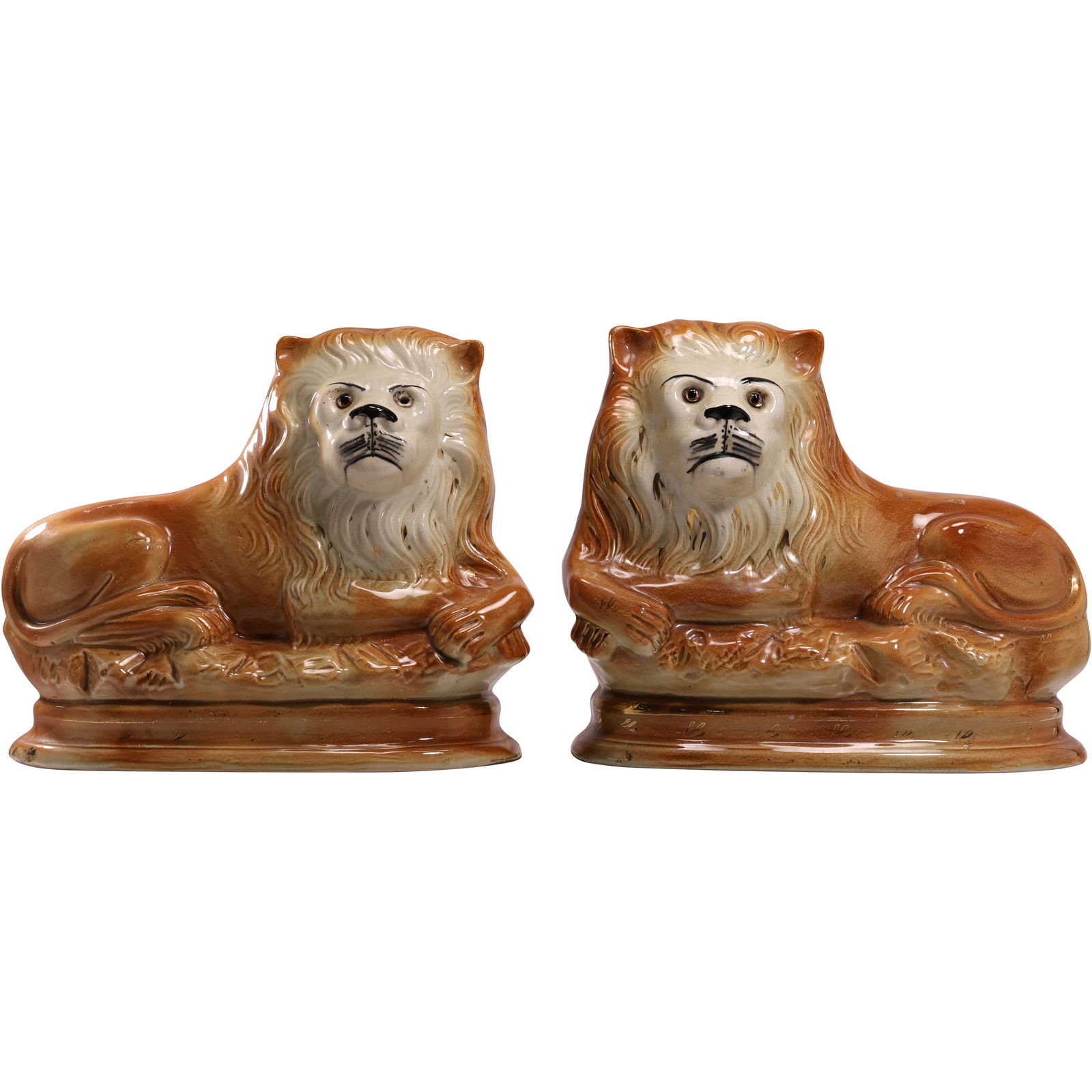 Pair of Antique English Staffordshire Mantle Lions: Pair of antique English Staffordshire mantle lions, each modeled in a regal reclining pose with finely detailed manes and expressive faces. The hand-painted glaze features warm amber and cream tones w