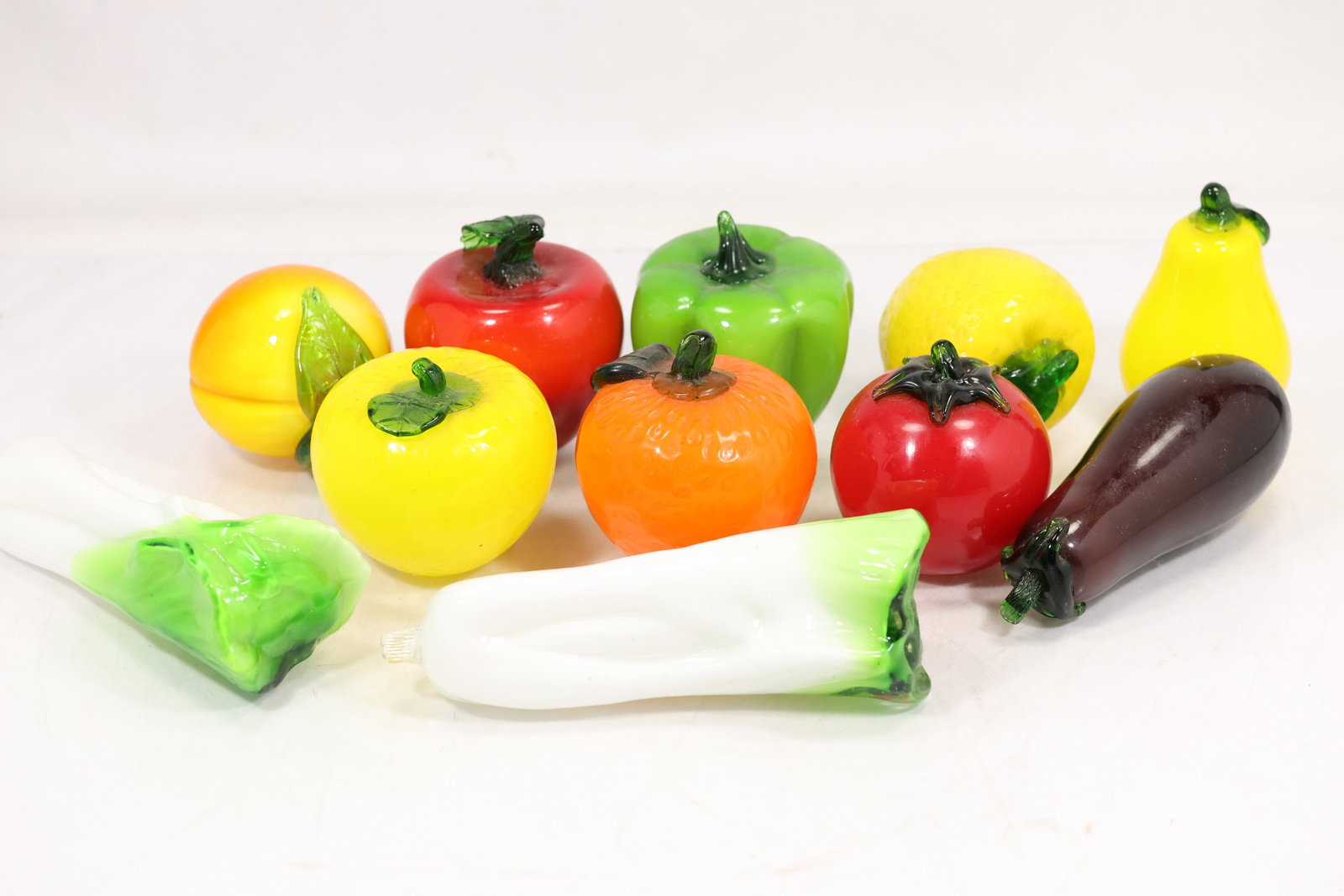 Collection of Hand Blown Art Glass Fruit and Vegetable Figurines: Colorful collection of hand blown art glass fruit and vegetable forms including apples, pears, citrus fruits, peppers, eggplant, and leafy vegetables. Each piece is crafted in vibrant translucent and 