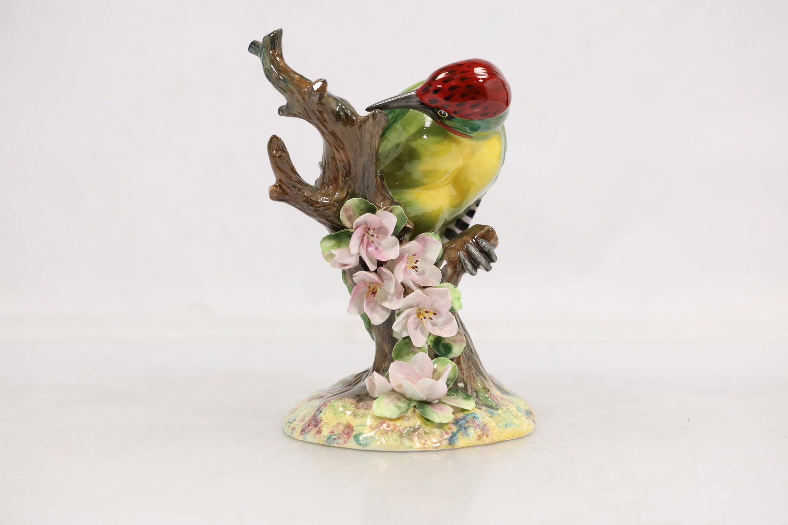 Royal Doulton Radnor Bone China Woodpecker Figurine, England: Charming Royal Doulton Radnor bone china figurine depicting a colorful woodpecker perched upon a flowering tree branch. Finely modeled and hand-painted with vibrant green plumage, a red crown, and bla