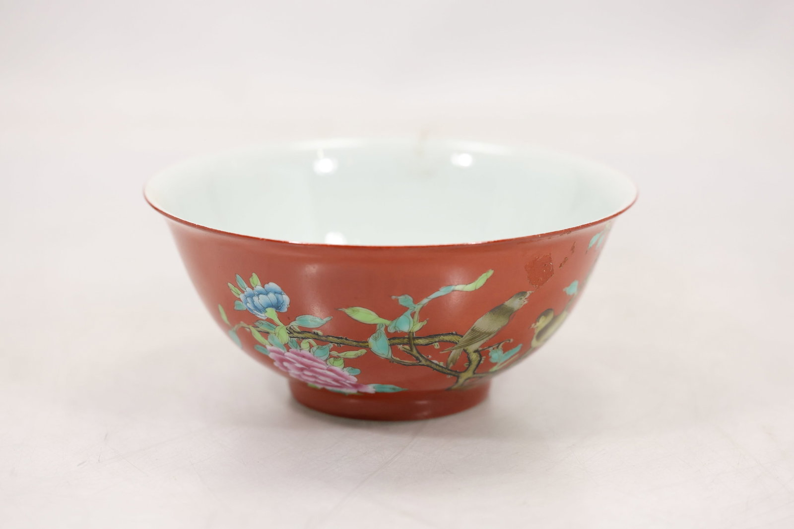 Chinese Porcelain Bowl with Iron-Red Ground and Floral Decoration: Chinese porcelain bowl featuring a vibrant iron-red exterior decorated with flowering branches, blossoms, and scrolling foliage rendered in famille rose-style enamels. Opposing the floral decoration i