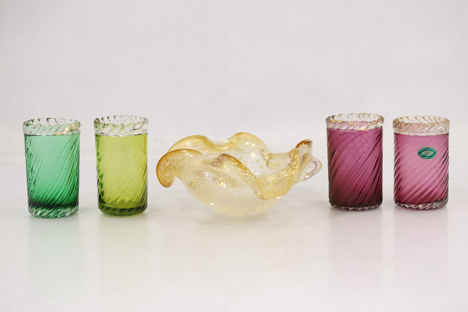 Italian Art Glass Tumblers and Gold Aventurine Bowl Five Pieces: Five piece Italian art glass group comprising four cylindrical tumblers in green lime and amethyst tones plus a folded clear and gold aventurine bowl. The tumblers have spiral optic bodies and
