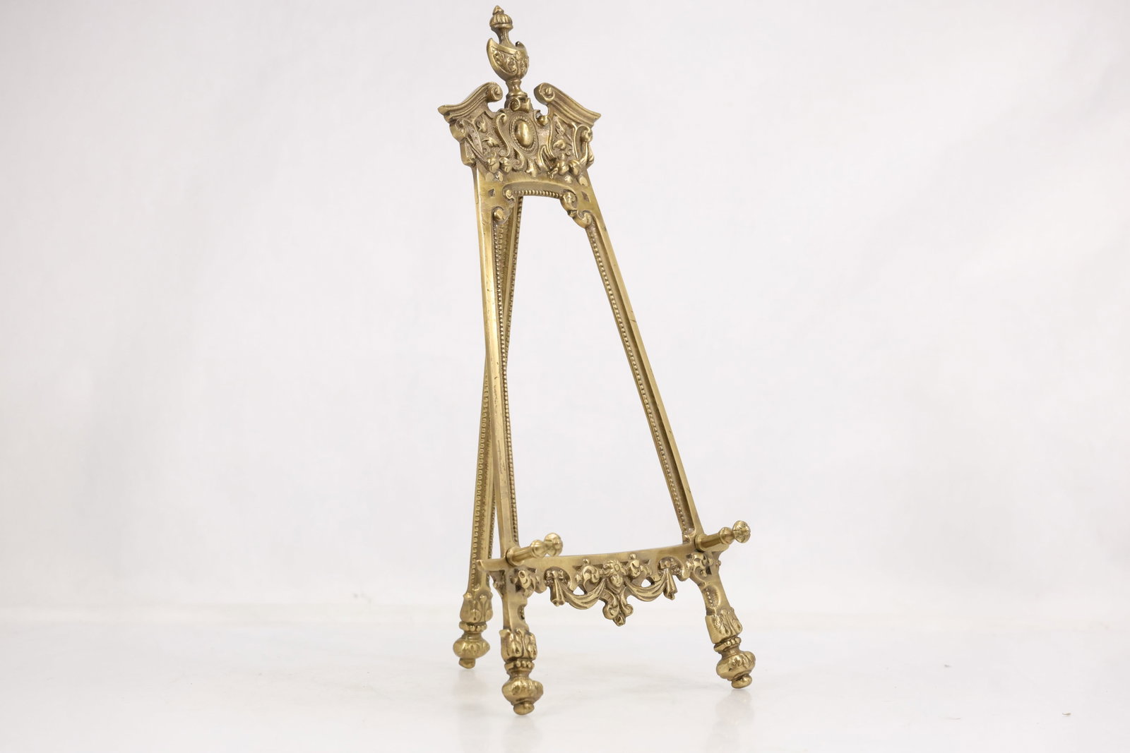 Ornate Rococo Revival Brass Tabletop Display Easel: Ornate cast brass tabletop display easel with pierced crest scrolling floral relief adjustable support pegs and three decorated feet. The folding rear support creates a freestanding display for a fram