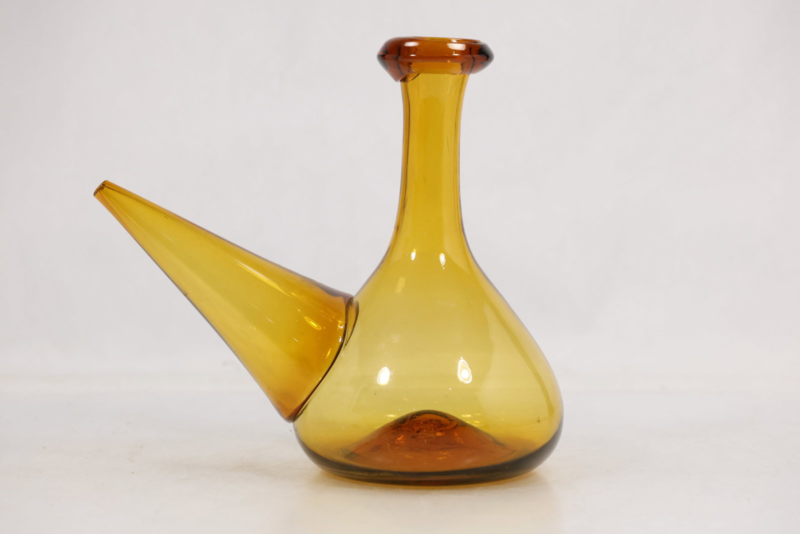 Amber Blown Glass Spanish Porron Wine Decanter: Amber blown glass porron wine decanter with rounded body tall bottle neck and long tapered side spout. The vessel has a warm translucent color applied rim and visible pontil area on the base. It is un