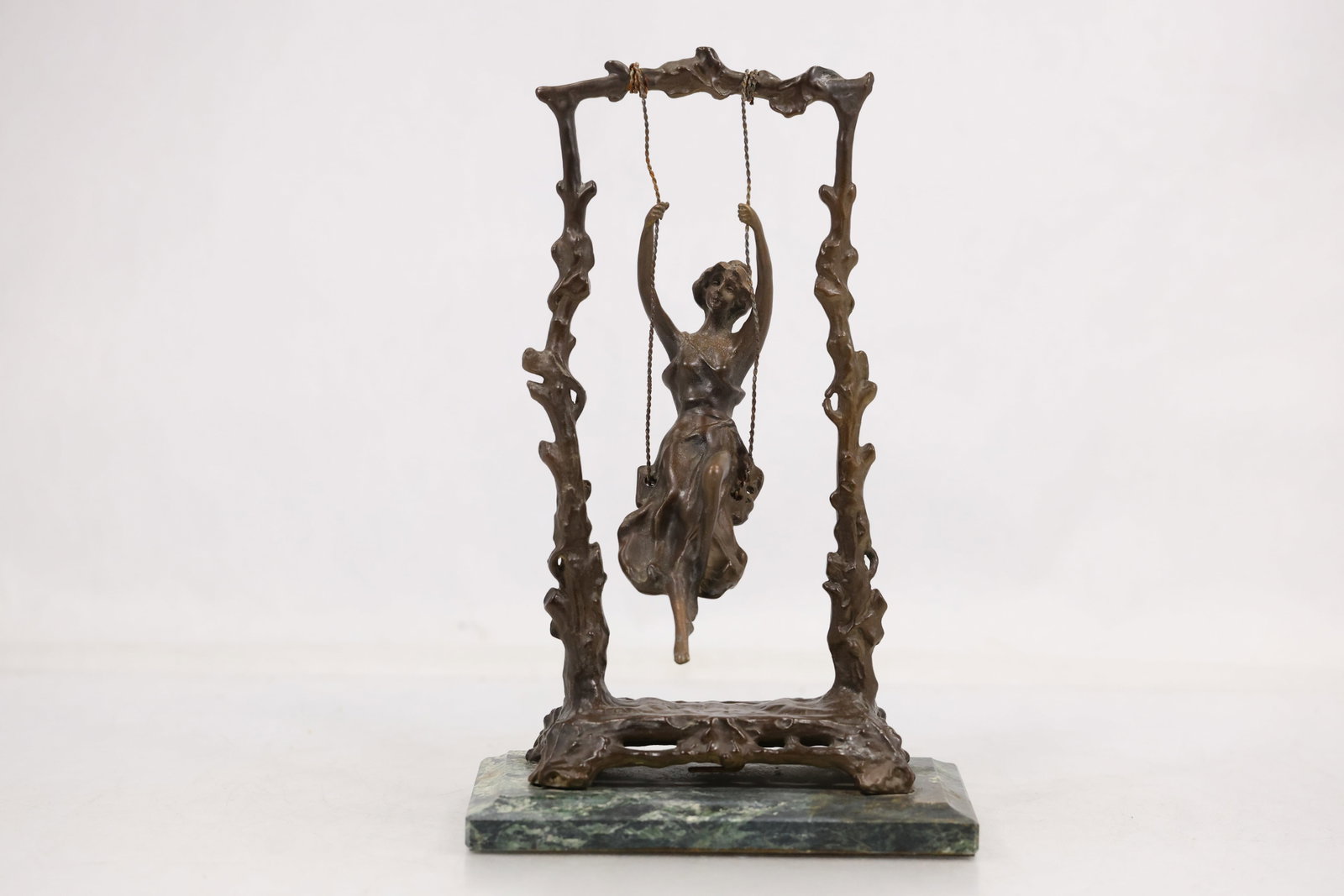 After Auguste Moreau Bronze Girl on Swing Sculpture: Bronze tone figural sculpture after Auguste Moreau depicting a young woman seated on a suspended swing above a naturalistic base. A cast signature appears along the base and the attribution is based