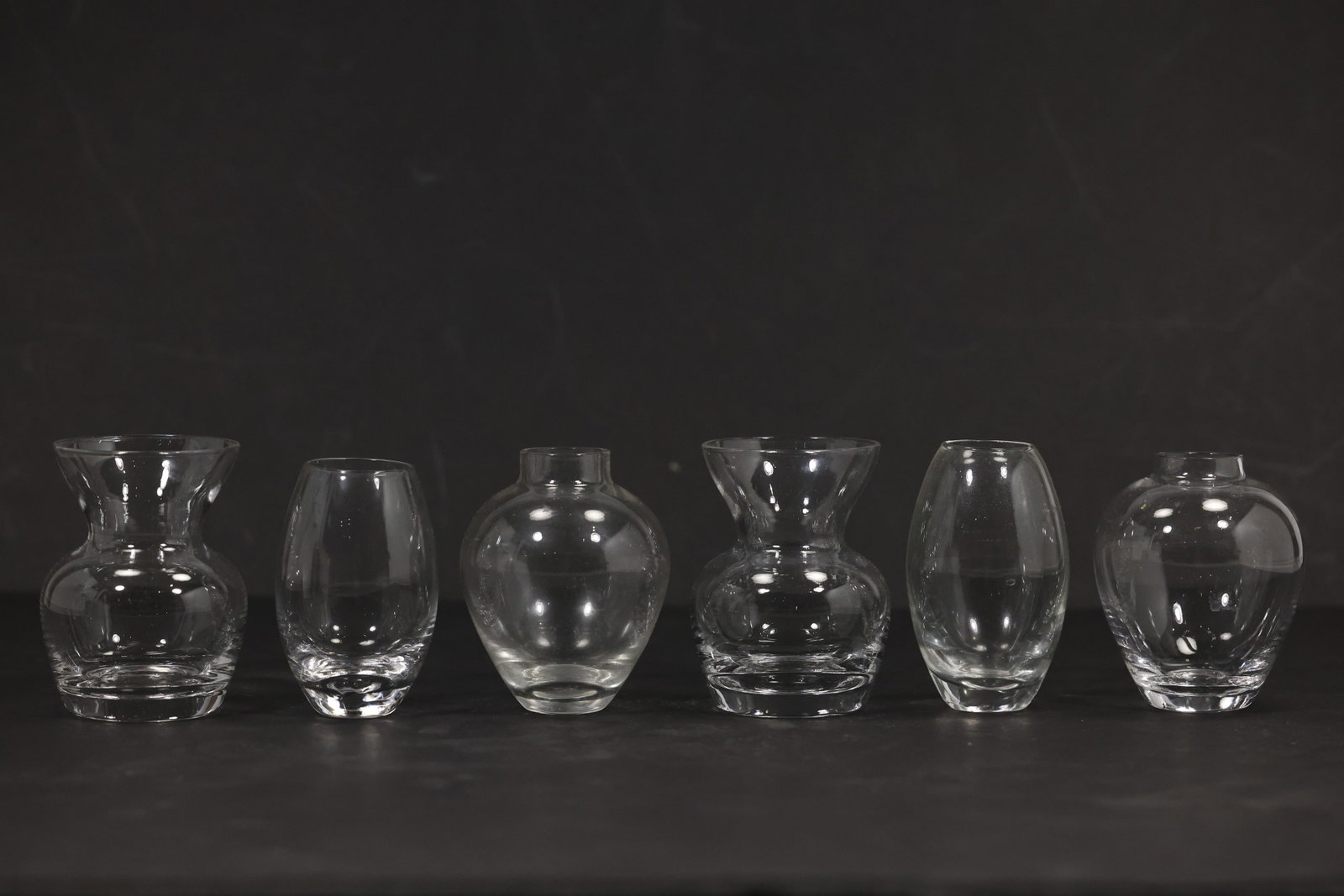 Six Assorted Clear Glass Bud Vases: Group of six small clear glass bud vases in varied bottle trumpet and flared forms. The vessels include molded and pressed surface patterns with narrow flower openings. The practical assortment