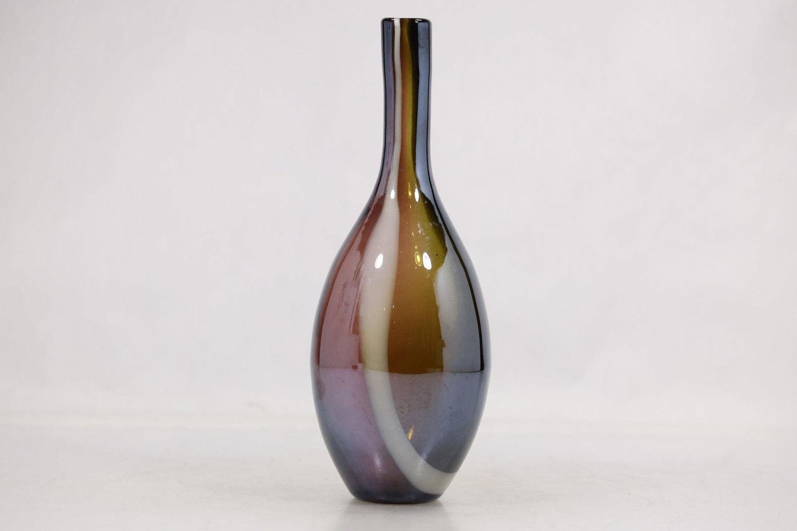 Multicolor Striped Art Glass Bottle Vase: Tall art glass bottle vase with a narrow neck and rounded body decorated in horizontal bands of olive green purple black and white. The surface has a glossy hand formed appearance and no visible
