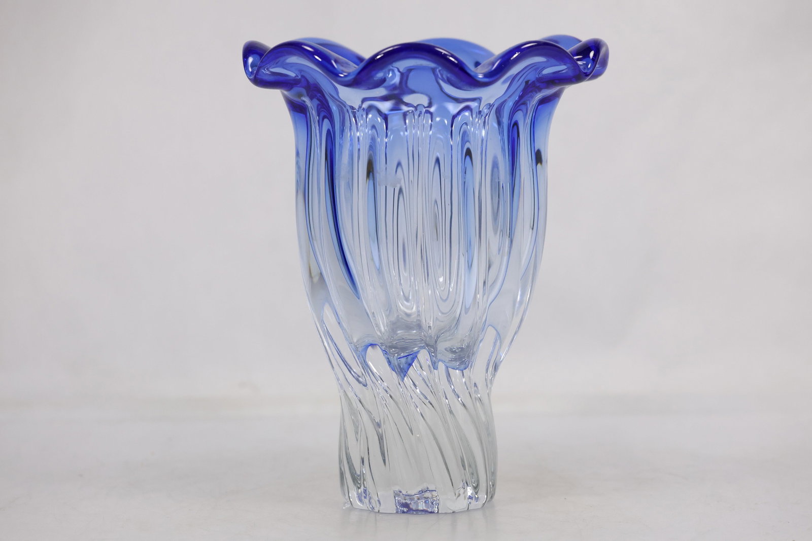Blue Ribbed Art Glass Ruffled Rim Vase: Blue clear art glass vase with a flared ruffled rim and vertically ribbed body. The vessel rises from a rounded foot and has a strong optical surface pattern. The fluid rim and saturated color relate