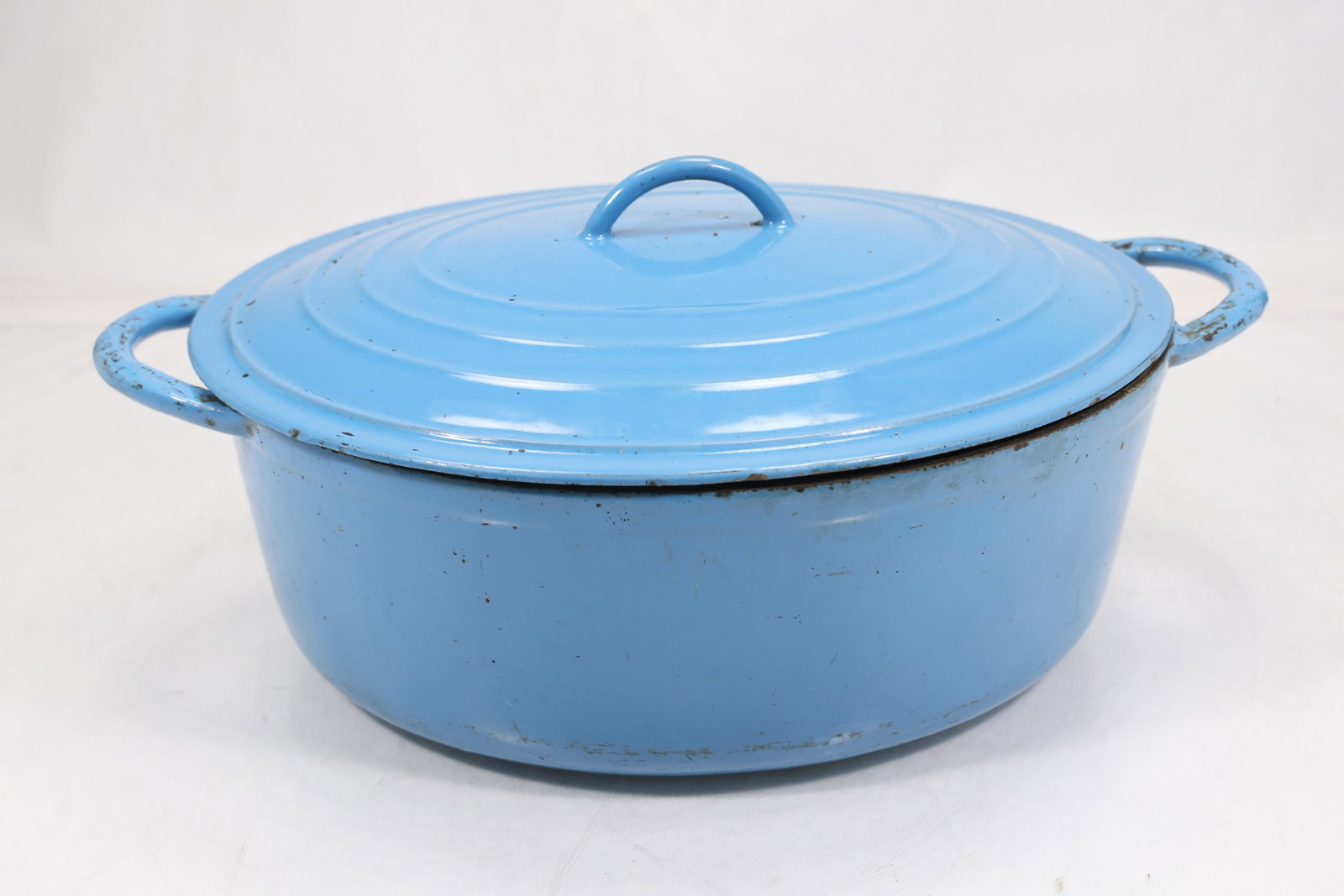 Blue Enameled Cast Iron Covered Casserole: Blue enameled cast iron covered casserole with a round body domed lid and two side handles. The heavy cooking vessel combines a glossy blue exterior with a dark rim. The durable form relates to French