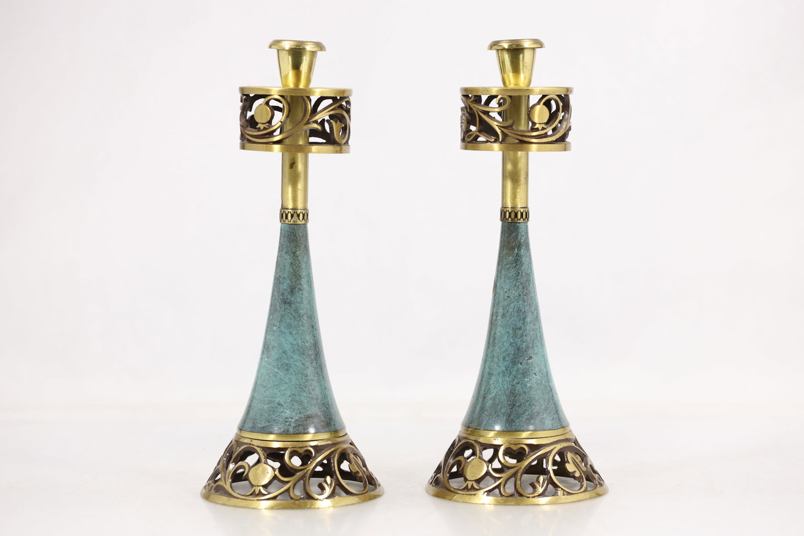 Pair Brass and Verdigris Openwork Candlesticks: Pair of tall candlesticks with verdigris tone tapered bodies and brass tone openwork bases and galleries. Each has a single raised candle socket and scrolling cutout decoration. The mixed metal palett