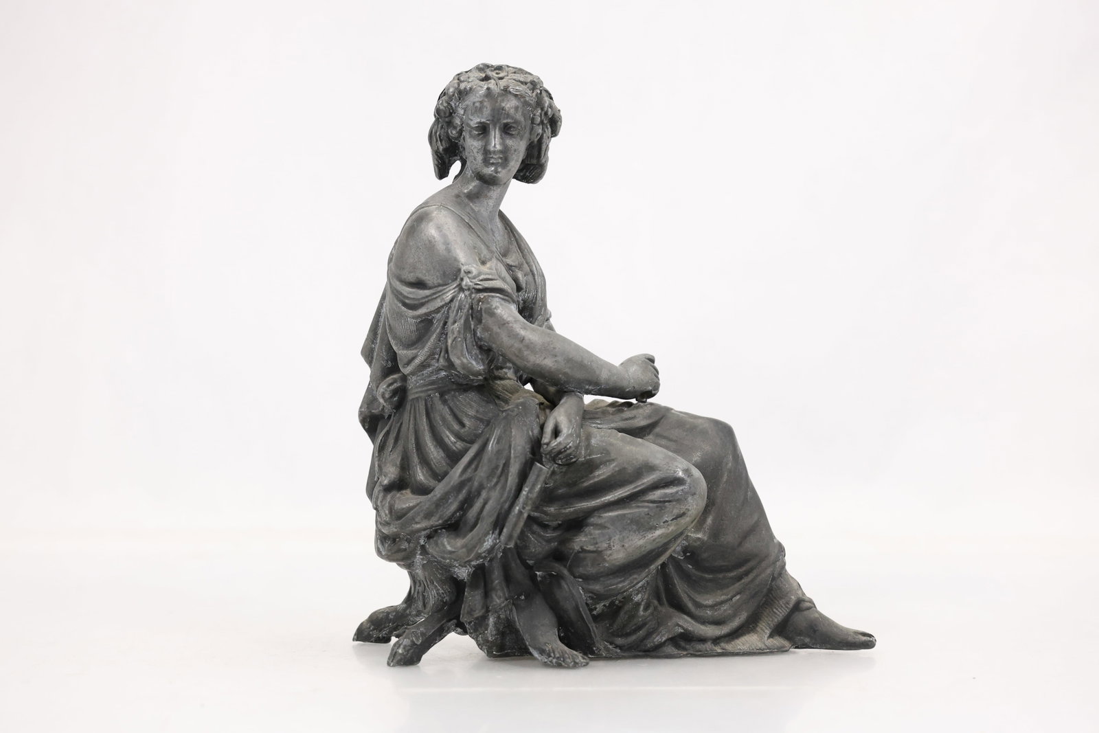 Classical Seated Female Figure Sculpture in Spelter Finish: Cast metal figure sculpture depicting a seated classical female figure draped in flowing robes and posed upon an integrated seat. The figure is rendered with detailed hair treatment and naturalistic f