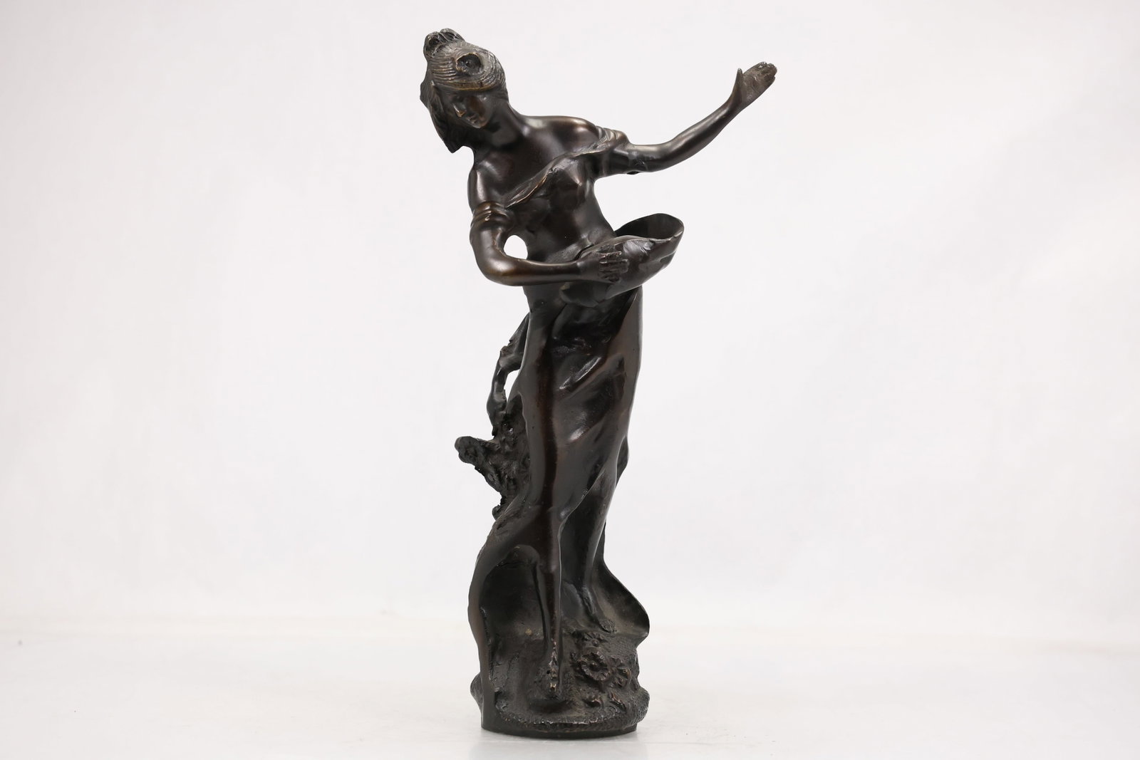 Bronze Art Nouveau Style Maiden Sculpture: Bronze sculpture depicting a graceful maiden in a flowing, wind-swept pose, rendered in the Art Nouveau tradition. The figure stands atop an organic naturalistic base with stylized foliage and flowing