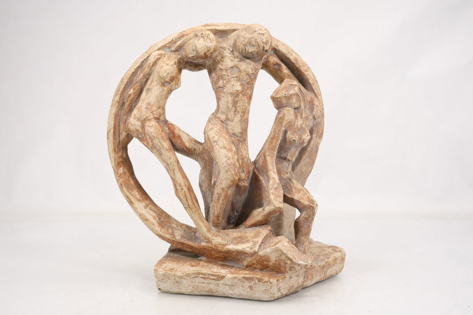 Abstract Figural Circle Sculpture of Entwined Figures: Cast composition sculpture depicting two stylized nude figures intertwined within an open circular tree like frame. The matte ivory and brown surface rests on a rectangular integral base. The