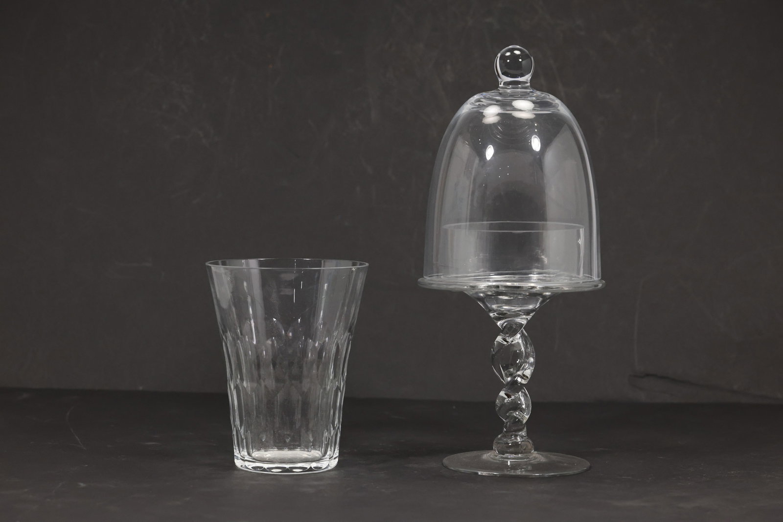 Orrefors Crystal Tumbler and Glass Cloche on Twisted Stem Stand: Two piece clear glass group comprising a faceted crystal tumbler signed Orrefors and a glass cloche raised on a pedestal with a twisted stacked glass stem. The cloche measures approximately 10 inches