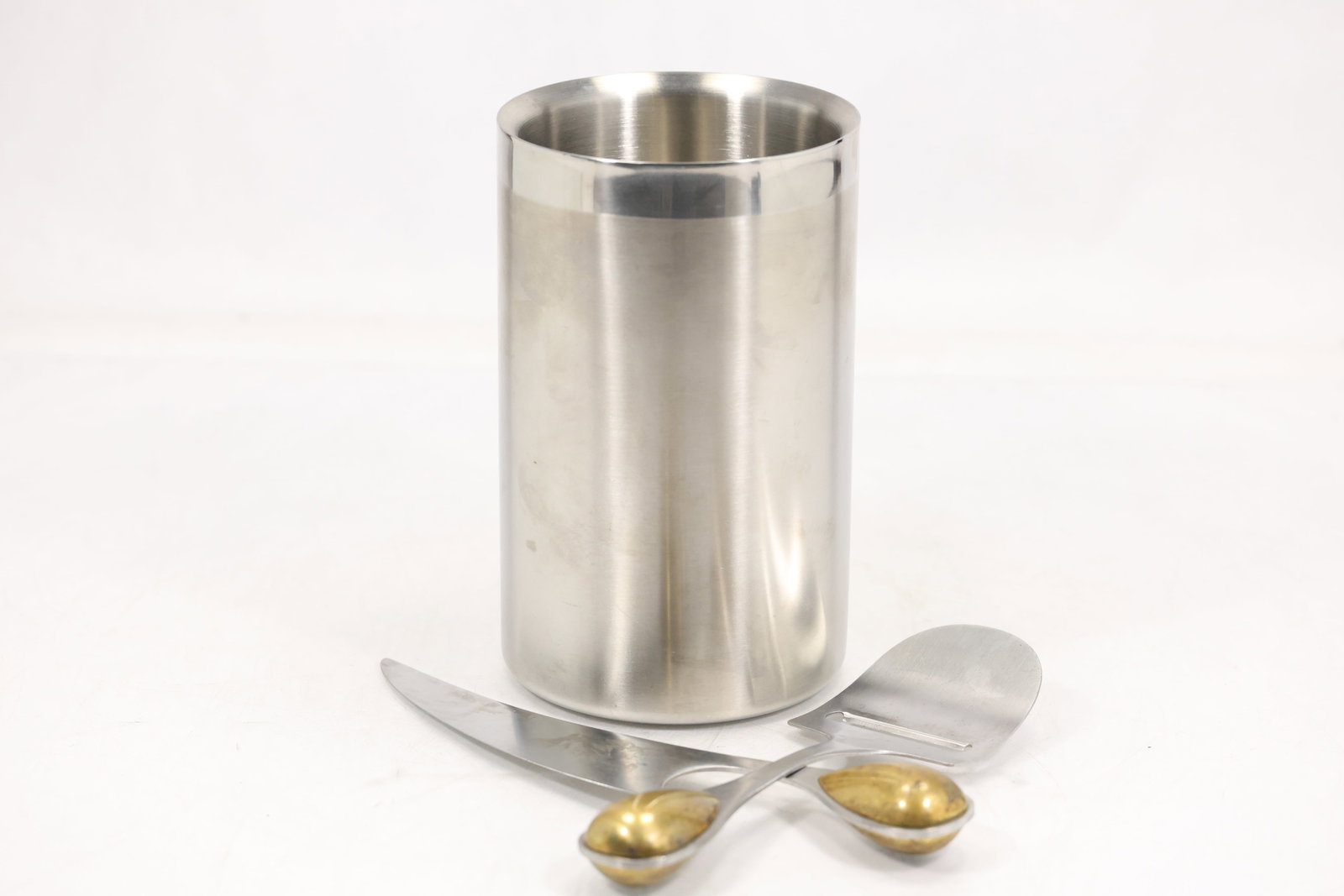 Dansk Stainless Steel Wine Cooler and Two Cheese Servers: Dansk stainless steel group comprising a double wall cylindrical wine cooler or utensil vessel and two cheese serving tools with brass tone teardrop terminals. The underside of the cylinder is marked