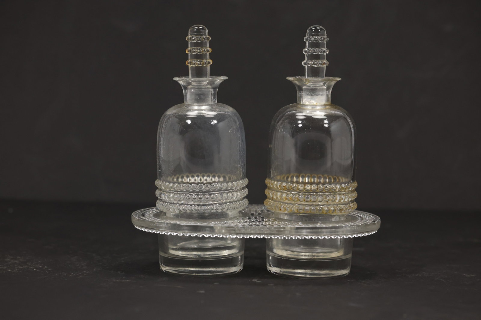 R Lalique Nippon and Tokyo Glass Cruet Set: R Lalique clear glass oil and vinegar cruet set in the Nippon and Tokyo patterns with matching ribbed stoppers and a fitted oval tray. Raised beaded bands encircle the lower bodies and the underside i