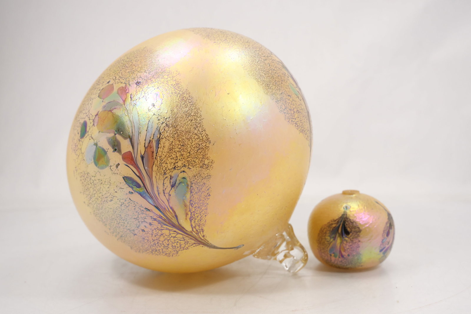 Two Iridescent Art Glass Floral Ornaments: Two iridescent art glass decorative forms comprising a large sphere and a smaller rounded vessel. Both are decorated with feathered floral patterns in gold pink green and dark tones. The lustrous surf