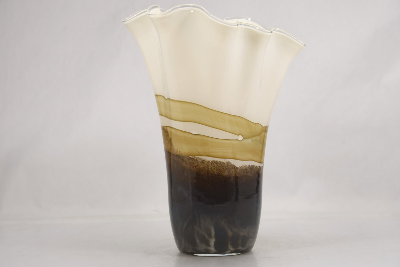 Hand Blown Art Glass Vase with Ruffled Rim in Amber Brown and White Tones: Hand blown art glass vase featuring a flared ruffled rim and elongated tapered form. The vase displays layered coloration with an opaque white upper section transitioning through amber tones into a da