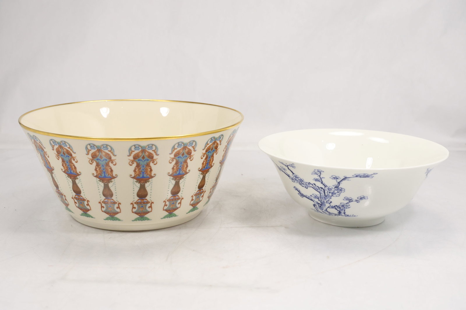 Pair of Porcelain Bowls with Egyptian Revival and Prunus Decoration: Pair of porcelain bowls comprising a cream ground bowl with gilt rim and repeating Egyptian Revival figures and vessels in blue red and green plus a white bowl decorated with a blue prunus tree motif.