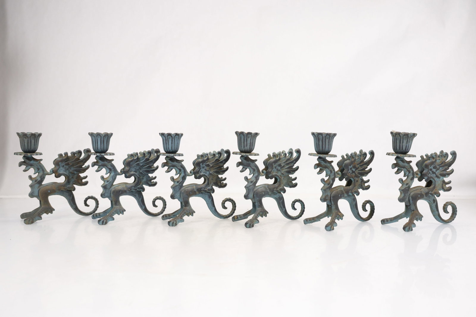 Set of Six Bronze Tone Chinese Dragon Candlesticks: Set of six cast metal candlesticks modeled as standing Chinese dragons supporting fluted candle cups. Each figure has an open mouth wing like crest curled tail and three footed stance. The surfaces ha