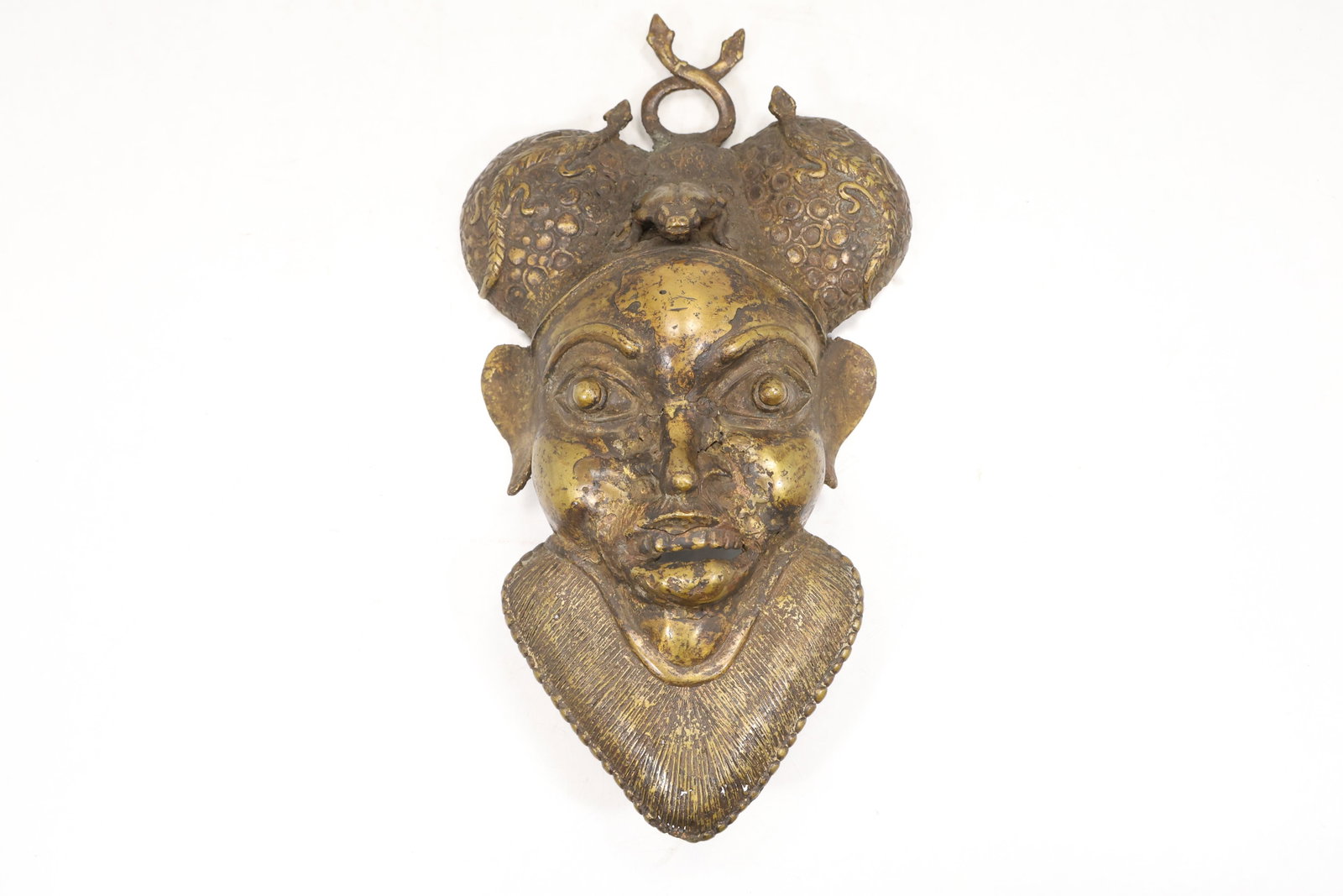 Cast Brass African Style Ceremonial Mask Plaque: Cast brass tone wall plaque in the form of an African ceremonial mask with an elongated face raised brows and patterned surface details. The reverse is formed for wall display. The stylized facial