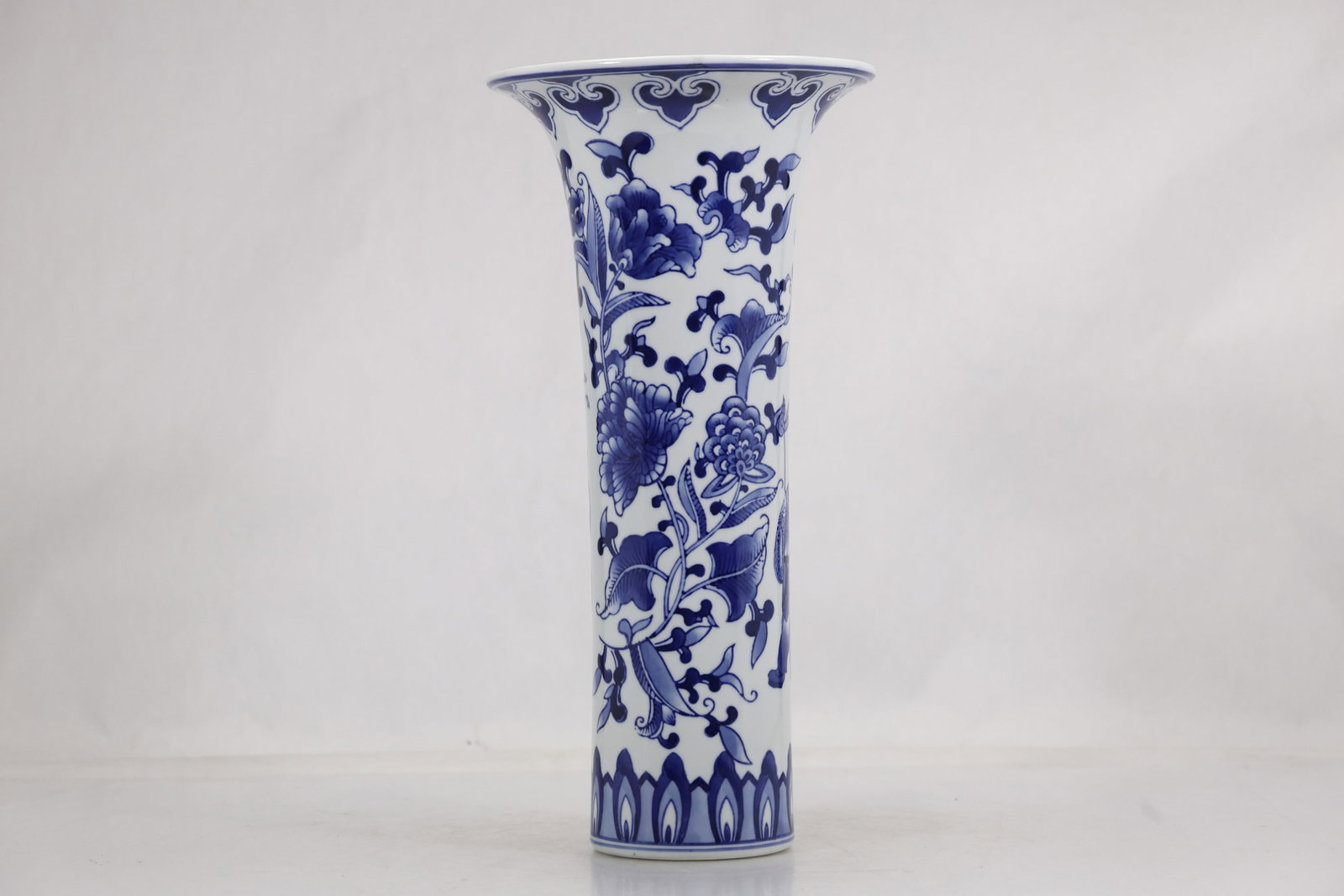 Bombay Blue and White Floral Porcelain Trumpet Vase: Tall blue and white porcelain trumpet vase decorated with scrolling flowers and foliage. The underside is marked Bombay Made in China. The floral palette draws from Chinese blue and white porcelain as