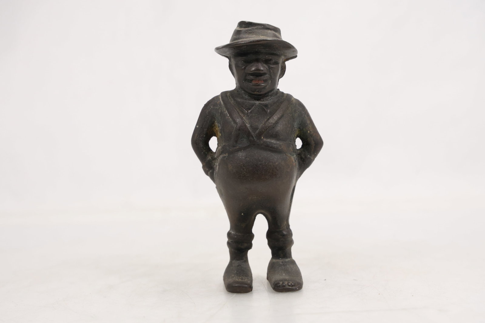 Cast Metal Figural Coin Bank: Dark cast metal figural coin bank modeled as a short standing man wearing a hat and period clothing. A coin slot is visible on the reverse. The novelty format relates to mechanical and still banks by