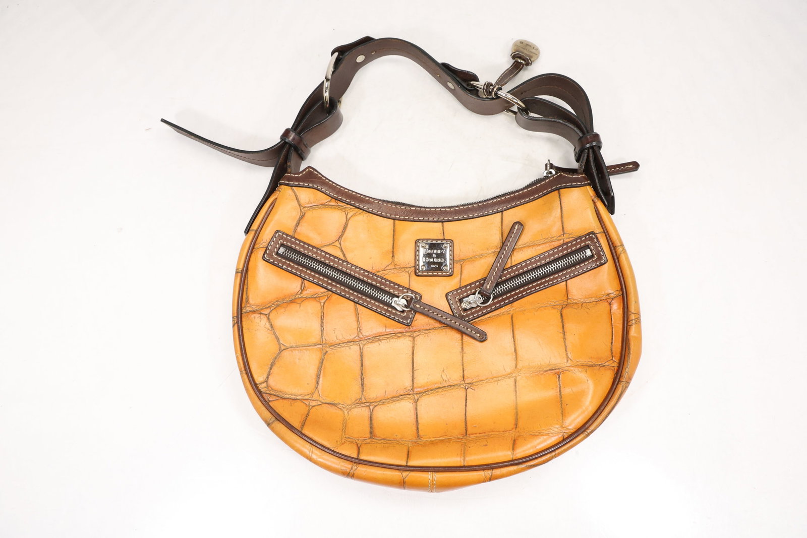 Dooney and Bourke Orange Embossed Leather Hobo Bag: Orange Dooney and Bourke hobo bag with embossed crocodile pattern brown leather trim adjustable shoulder strap and two angled front zip pockets. A metal Dooney and Bourke 1975 plaque is applied to the