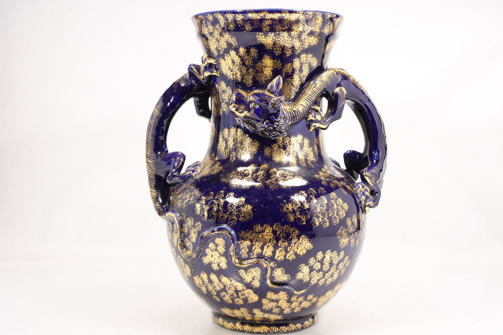 Blue and Gilt Chinese Dragon Handle Porcelain Vase: Large cobalt blue porcelain vase with two sculptural dragon handles and raised dragon decoration across the rounded body. Mottled gilt decoration covers the blue glazed surface. The modeled dragons dr