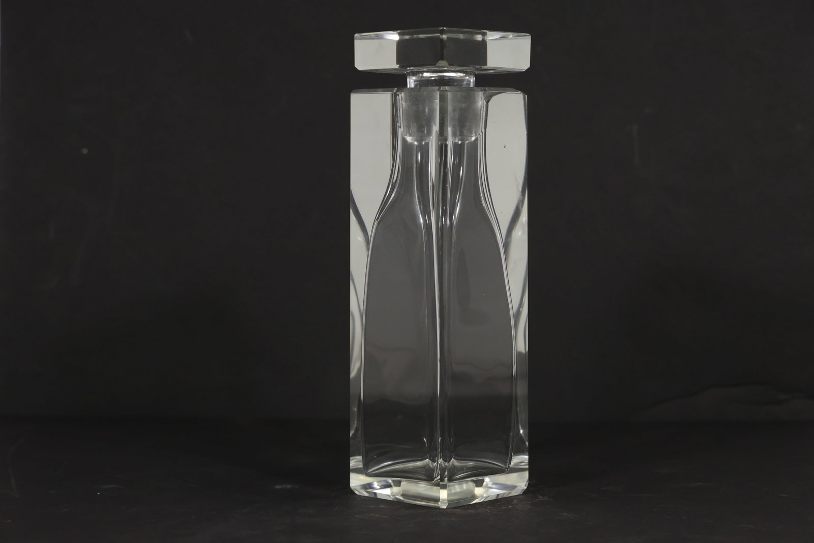 Clear Crystal Square Decanter with Stopper: Heavy clear crystal decanter with a tall square body curved inner contours and a large faceted square stopper. Polished geometric surfaces create strong optical reflections. The architectural form