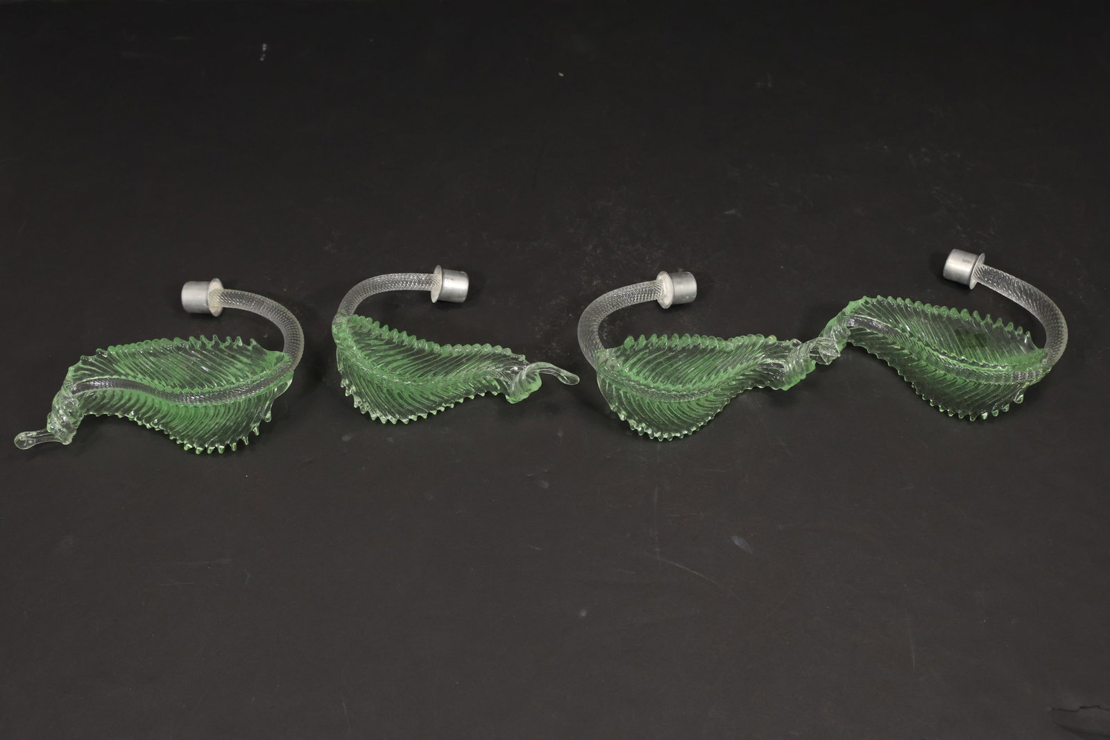Set of Four Green Murano Glass Leaf Chandelier Parts: Set of four vintage mid century Murano glass green foliage chandelier replacement parts from confirmed importer stock. Each piece has a short curved stem and a ribbed leaf body with serrated contours 