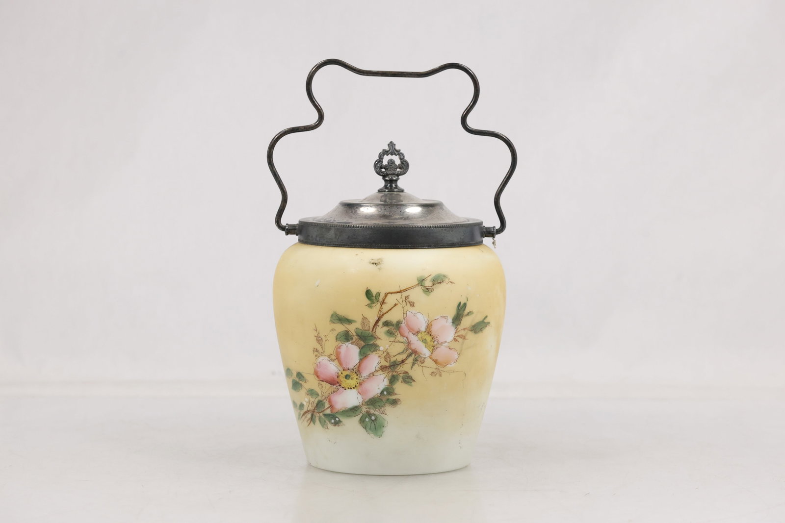 Hand Painted Satin Glass Biscuit Jar with Pewter Lid and Handle: Satin glass biscuit jar or covered dresser jar featuring a soft ivory to pale yellow ground with hand painted floral decoration. The body is decorated with pink blossoms green leaves and trailing stem