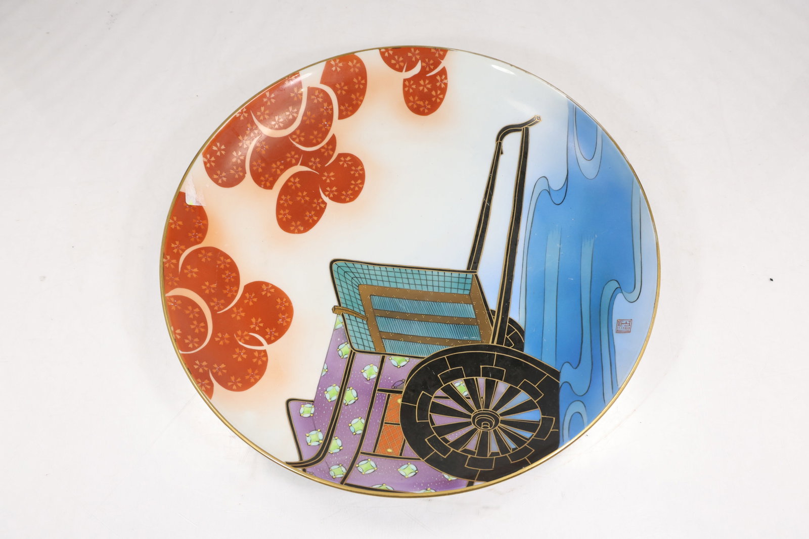 Large Modern Graphic Porcelain Charger: Large round porcelain charger decorated with a colorful graphic composition of a cart wheel and abstract orange blue black and white forms. The shallow plate has a broad display surface. The bold post