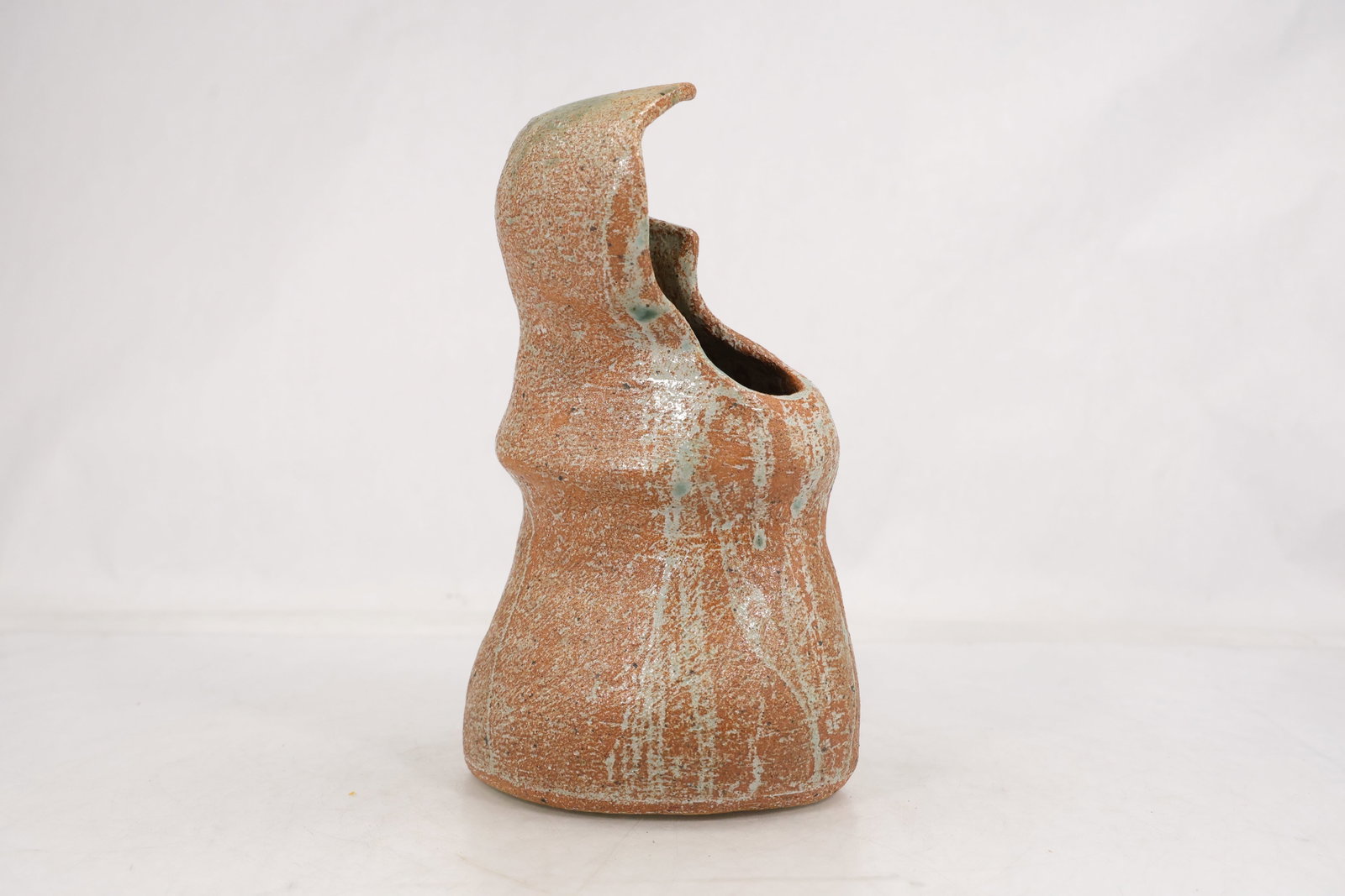 Mid Century Studio Pottery Bird Sculpture: Mid century studio pottery sculpture modeled as a stylized bird with an upright head curved beak and rounded body. The warm brown and tan surface has a softly textured glaze and the photographed under