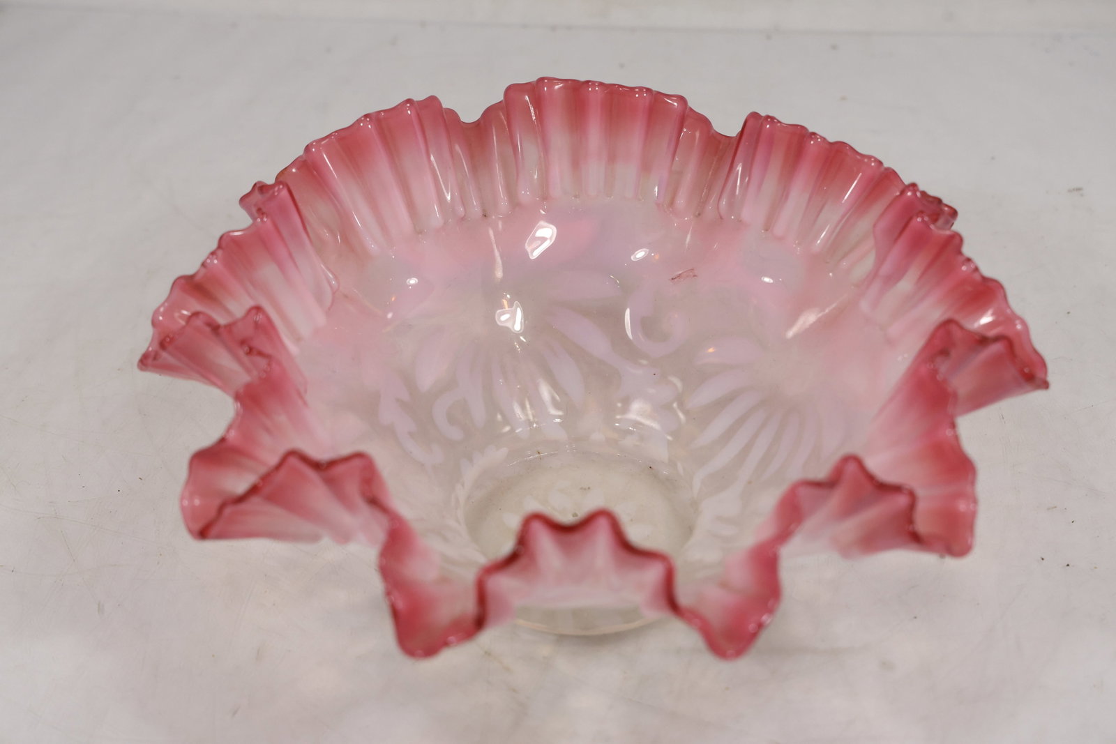 Pink Opalescent Ruffled Glass Bowl with Molded Floral Pattern: Pink opalescent glass bowl featuring a wide ruffled rim and molded decorative pattern. The bowl displays a translucent white center transitioning to deeper pink coloration along the crimped and undula