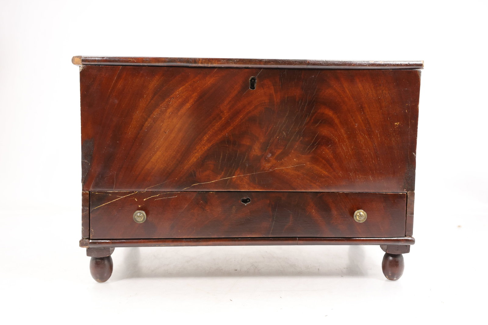 Miniature Mahogany Veneer Blanket Chest with Drawer and Bun Feet: Miniature wooden blanket chest form storage box with mahogany tone veneer a rectangular hinged lid and a deep open interior. A full width lower drawer has two round pulls and key openings while four t