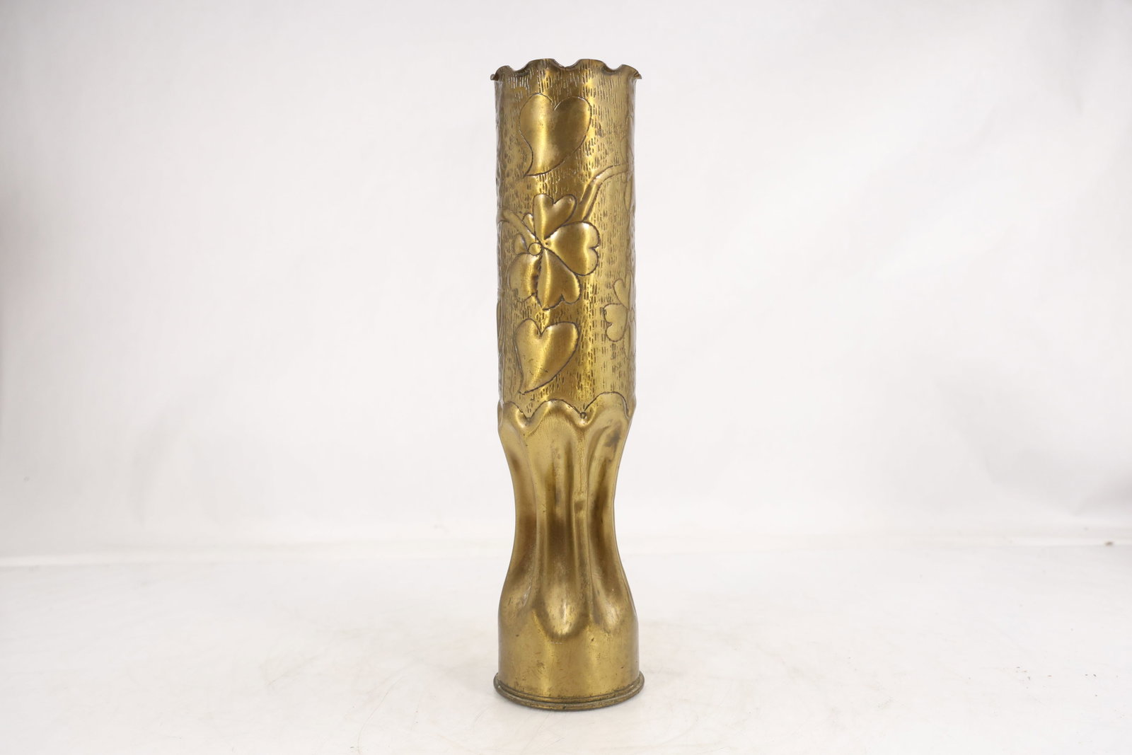 Nouveau Style Repousse Brass Vase with Floral Decoration: Tall brass vase with a cylindrical upper body and flared organic form at the lower section. The exterior is decorated in relief with stylized floral and foliate motifs extending vertically along the b