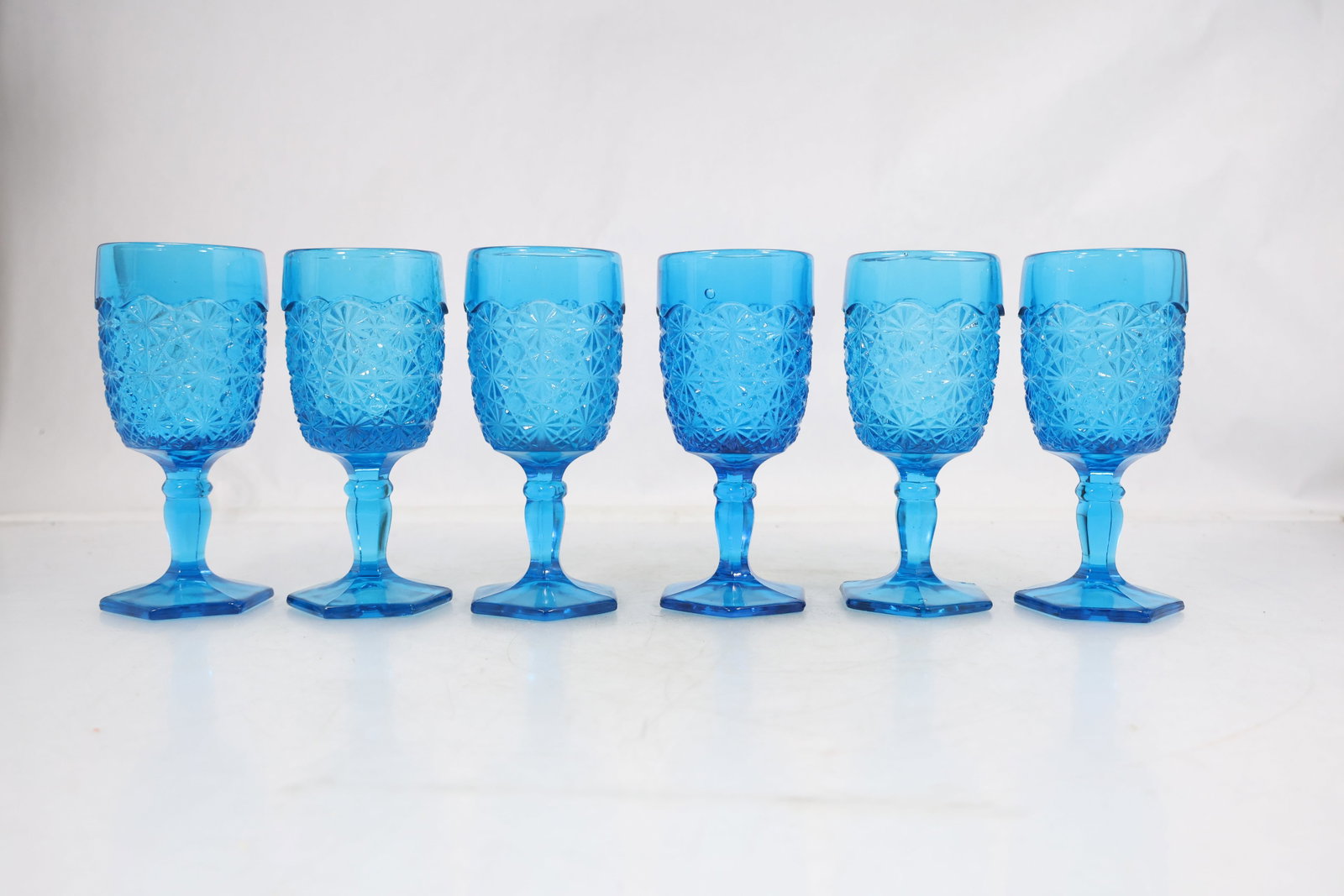 Set of Six Blue Pressed Glass Goblets with Daisy and Button Pattern: Set of six blue pressed glass goblets featuring a molded geometric floral pattern commonly referred to as daisy and button. Each goblet is formed with a panel of repeating starburst and diamond motifs