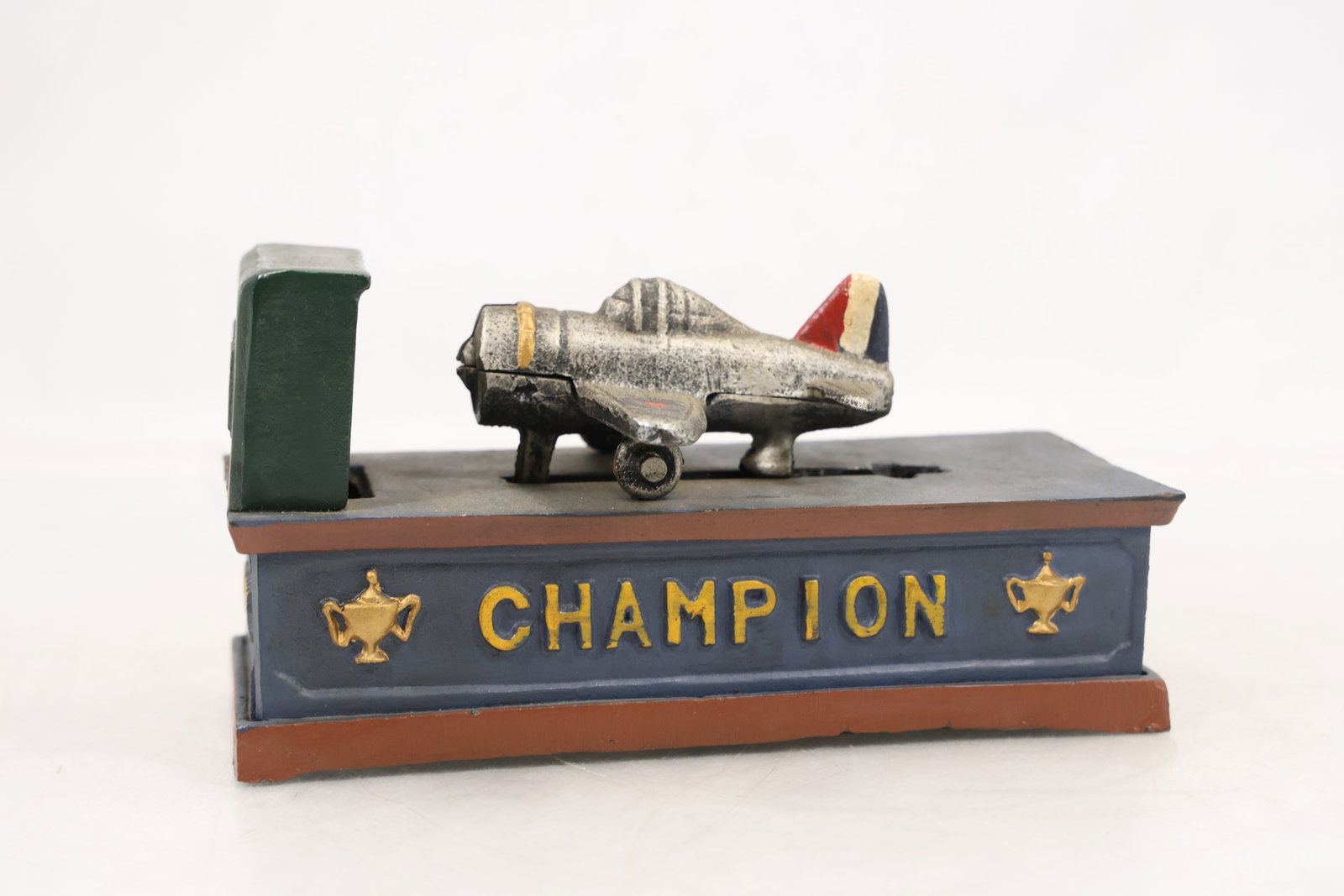 Vintage Cast Iron "Racing Ace" Champion Mechanical Airplane Coin Bank: Vintage mechanical coin bank featuring a cast metal airplane mounted on a painted base marked “Champion,” commonly associated with the Racing Ace aviation theme. Designed with classic early-to