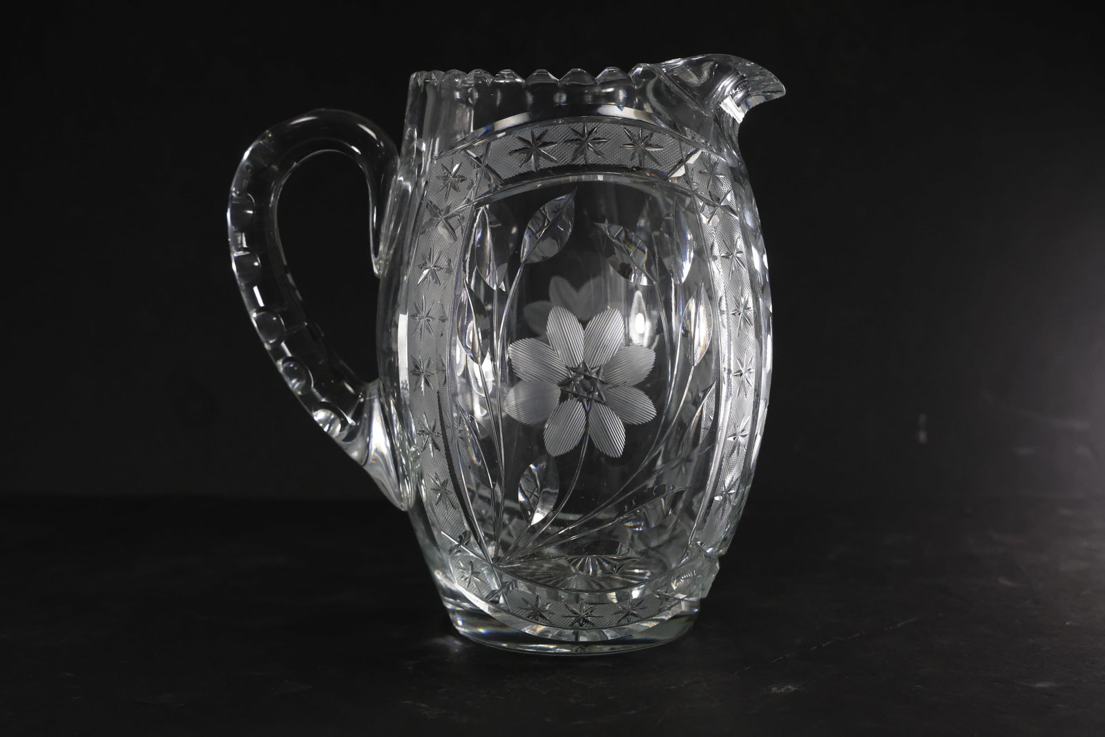 American Brilliant Style Clear Glass Pitcher: Heavy clear glass pitcher in the American Brilliant style, featuring an intricate cut pattern with a central floral motif. The body displays a combination of deep geometric cuts and crosshatching, cat