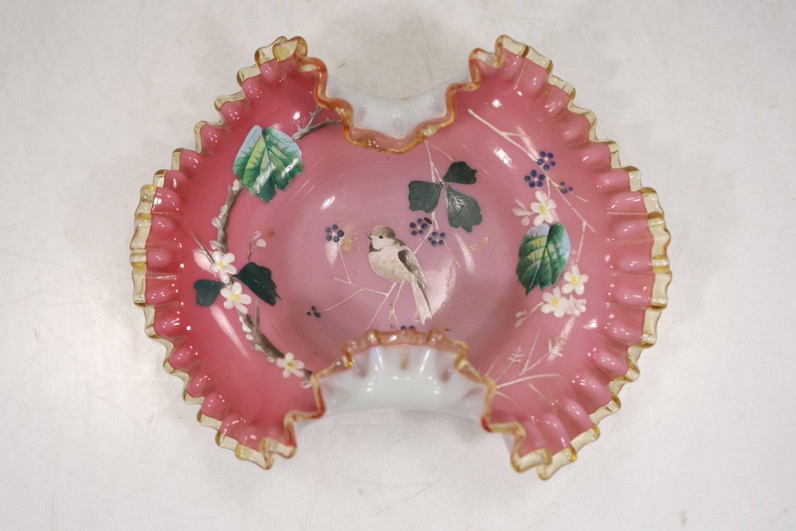 Hand Painted Cranberry Floral and Bird Design Bride's Basket Bowl: Decorative cranberry glass bride’s basket bowl featuring a ruffled, crimped form. The body is hand-painted with a delicate floral and bird design, accented with soft enamel colors and gold trim alon