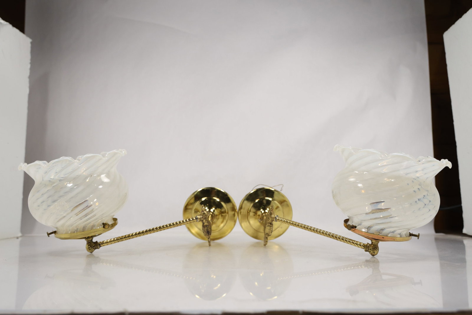 Pair of Brass Swing Arm Wall Sconces with White Spiral Shades: Matching pair of wall-mounted brass sconces featuring adjustable swing arms and white spiral-pattern glass shades. The shades have a twisted, flared form that adds a bit of movement and texture, while