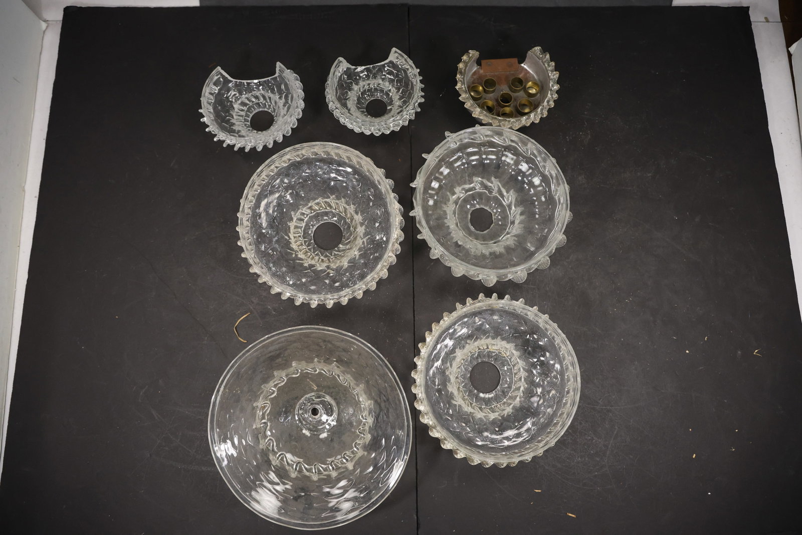 Set of Seven Clear Murano Glass Chandelier Shades: Set of Seven vintage mid century Murano glass chandelier shades from confirmed importer stock. Photographs show flared or domed bodies with central apertures and decorative rims in clear tones.