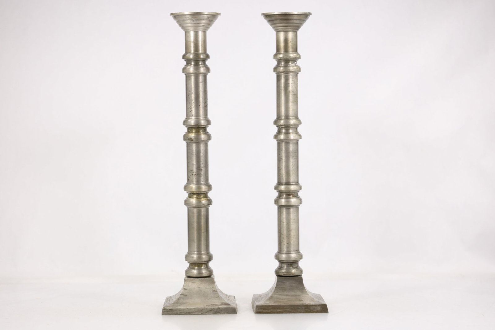 Pair Silver Tone Metal Candlesticks: Photographs show pair silver tone metal candlesticks in cast or worked metal with modeled ornament and a patinated or polished surface. The subject and construction are stated without an unsupported m