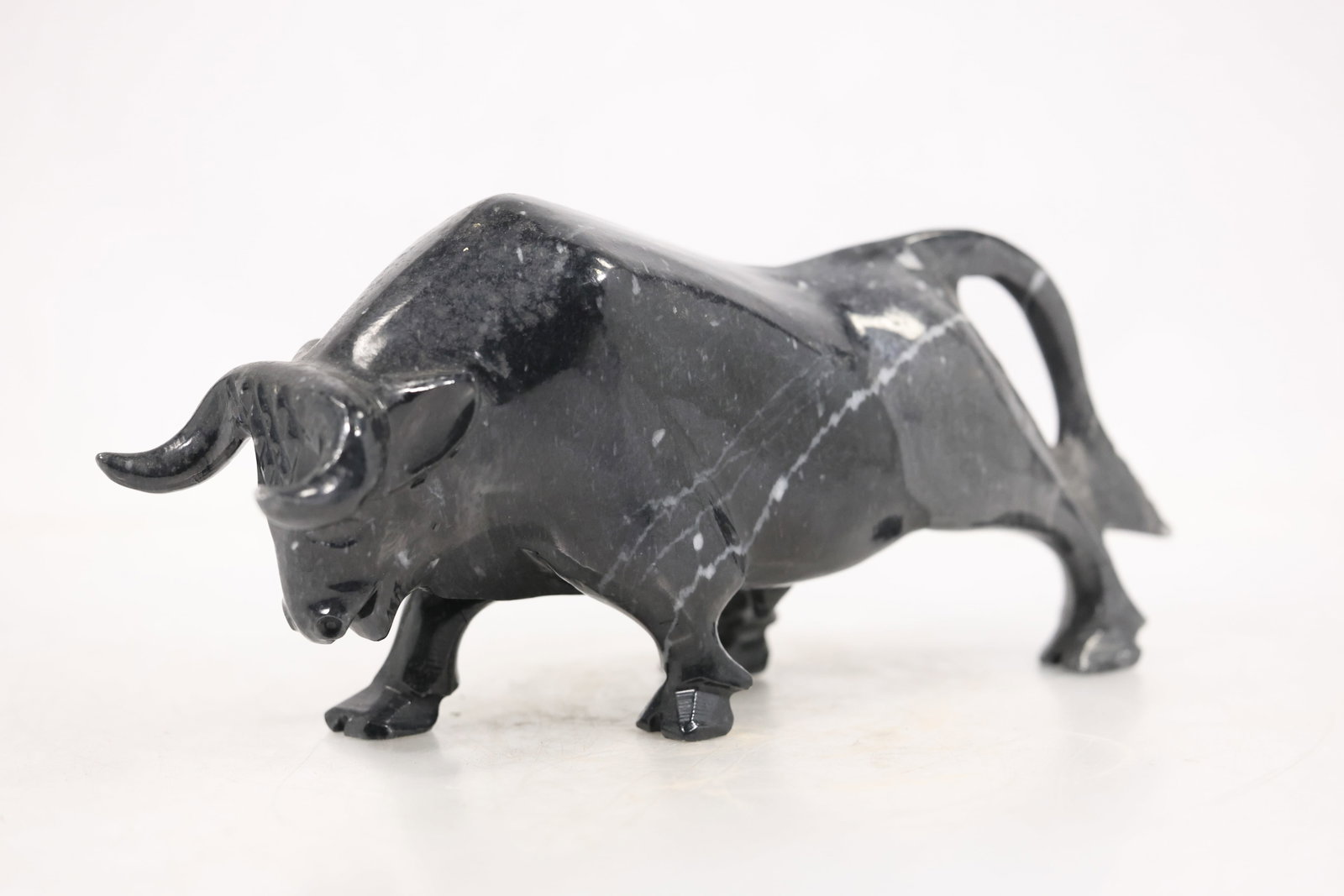Carved Gray Marble Charging Bull Sculpture: A carved gray marble sculpture depicts a charging bull with lowered head forward horns and a compact muscular body. Natural white veining passes through the polished stone and no artist signature is c